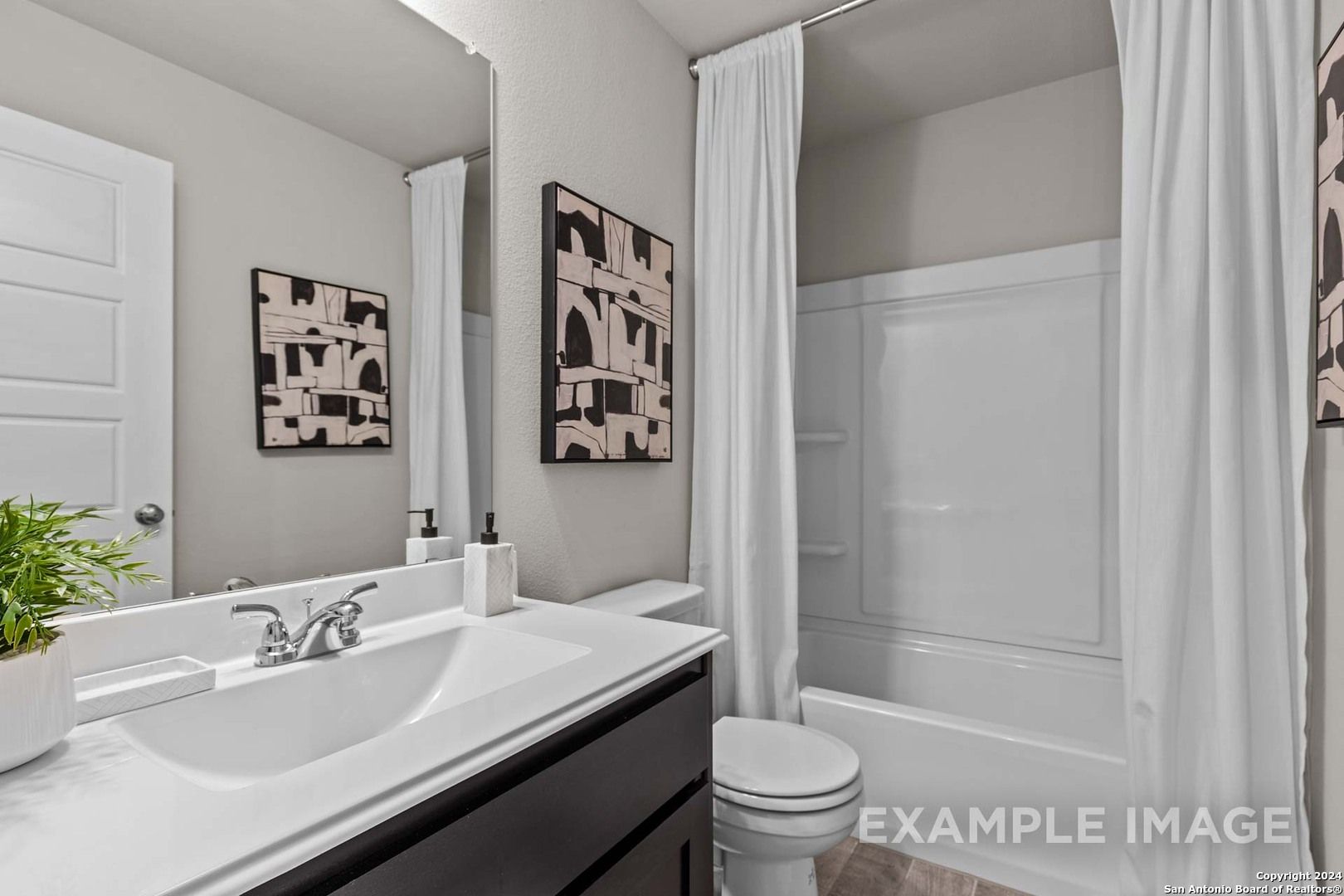 Modern bathroom with white tub-shower combo, sleek black vanity, large mirror in Davidson Homes The Collin A, Seguin, Texas