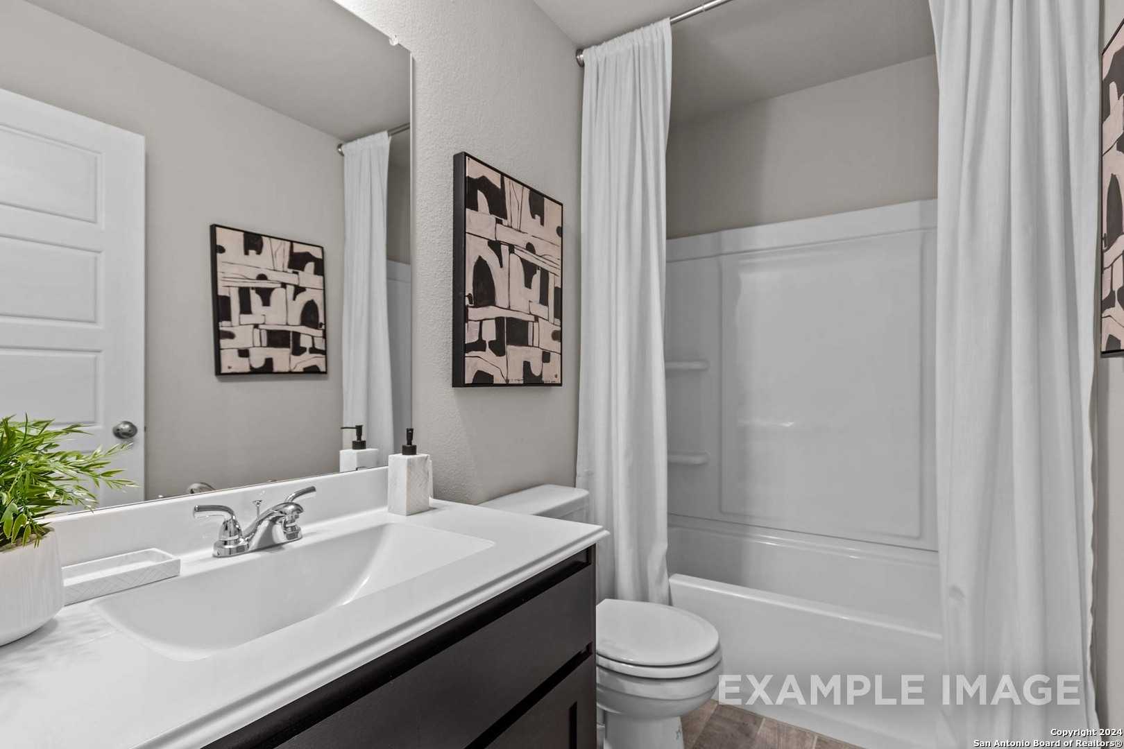 Modern bathroom with white tub-shower combo, sleek black vanity, large mirror in Davidson Homes The Collin A, Seguin, Texas