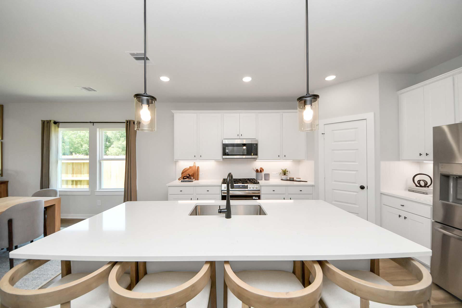 Modern kitchen with white cabinets, large island, and pendant lighting at The Enclave at Newport in Crosby, Texas.