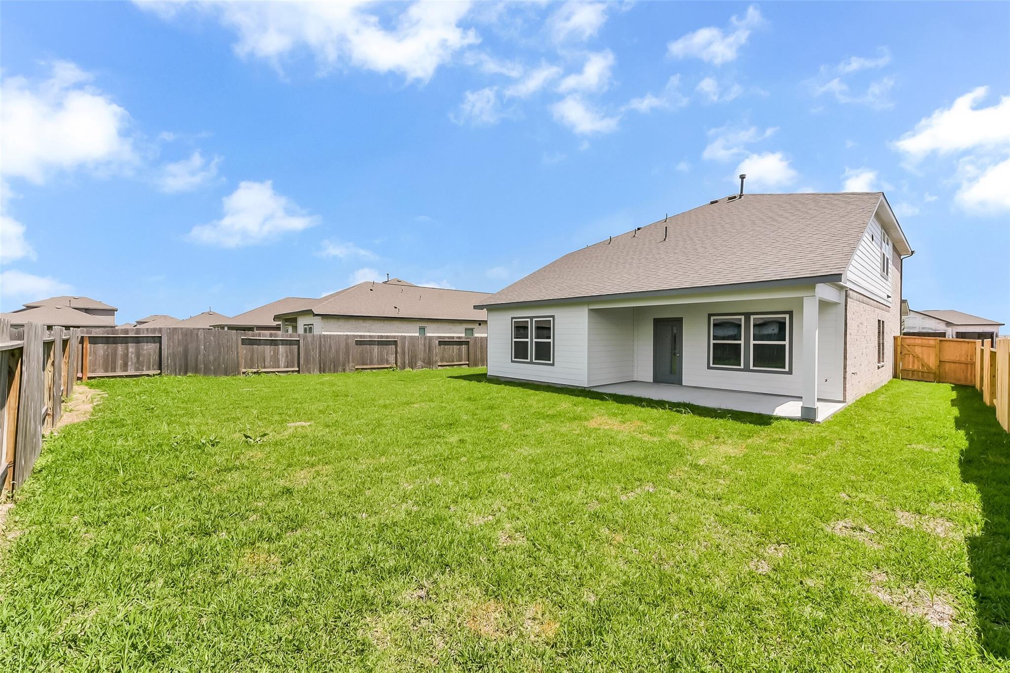 White-sided two-story home with brick accents, covered patio, and lush green yard in River Ranch Meadows, Dayton, Texas