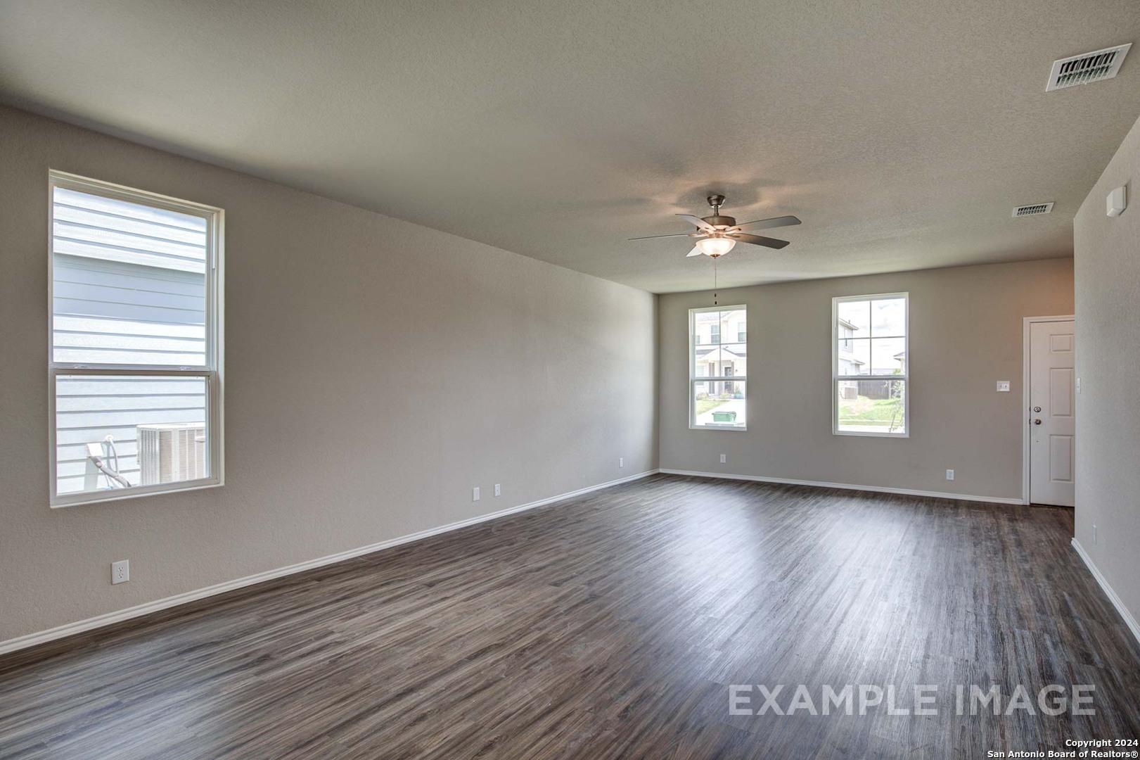 Spacious living room with hardwood floors, beige walls, and large windows in Davidson Homes The Murray J, Bricewood, San Antonio