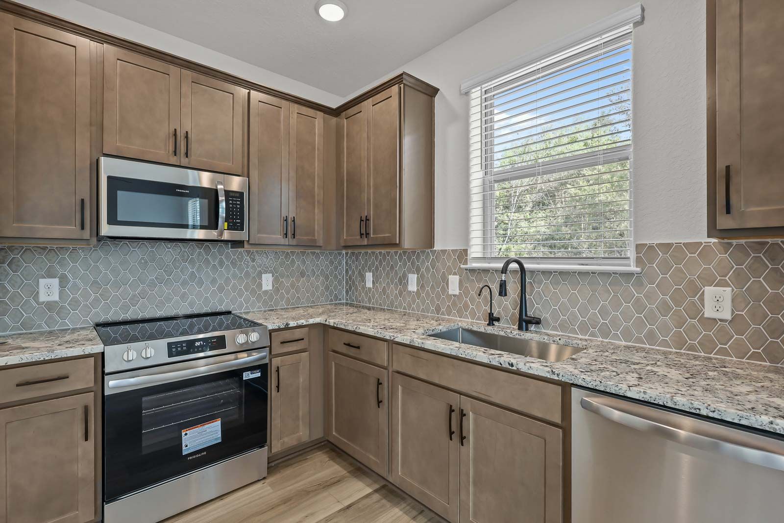 Modern kitchen in The Florence B featuring granite countertops, stainless steel appliances, and stylish hexagon backsplash.