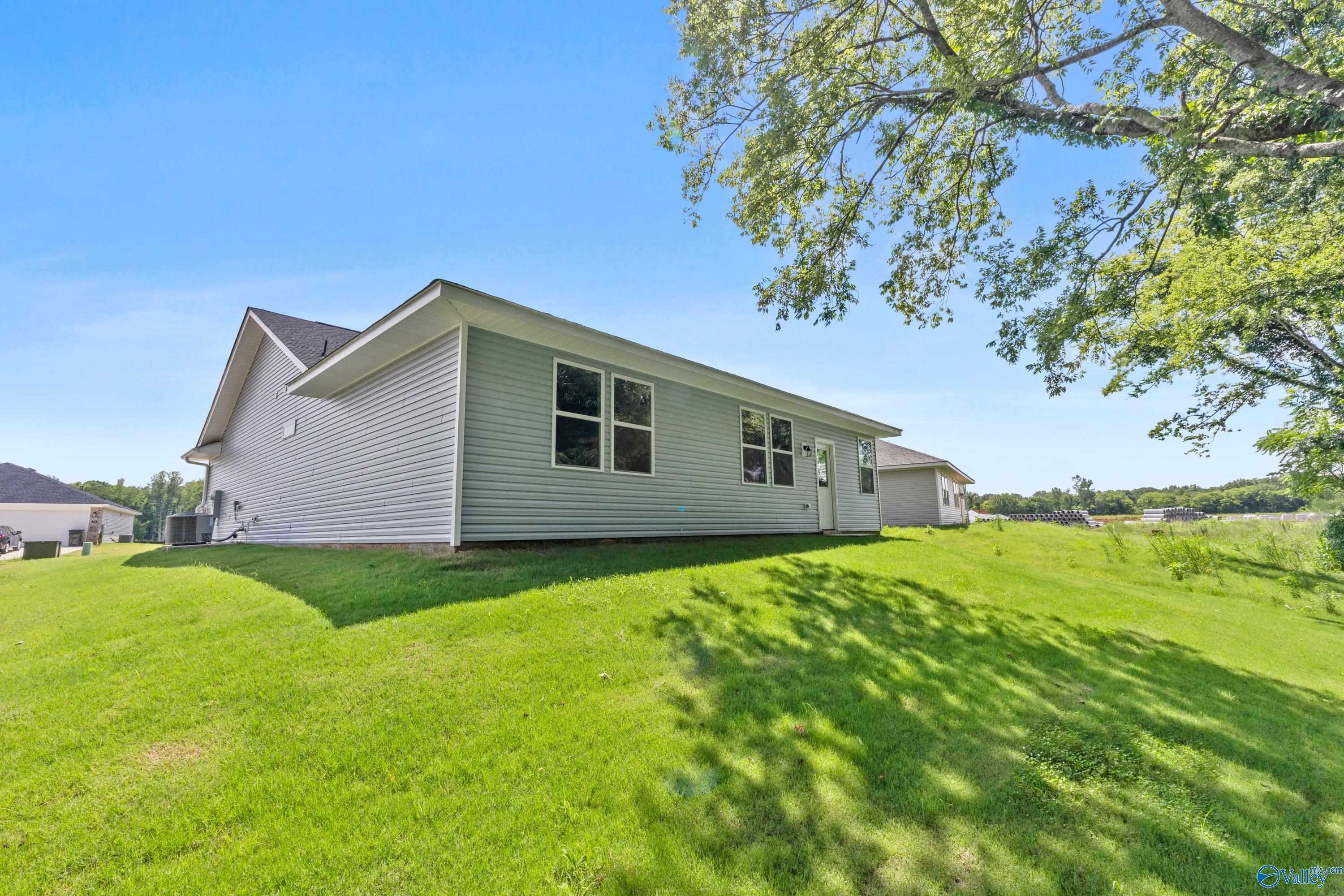 Exterior side view of The Phoenix 1-story home by Davidson Homes in Forest Glen, Hazel Green, Alabama, with light gray siding and lush green lawn