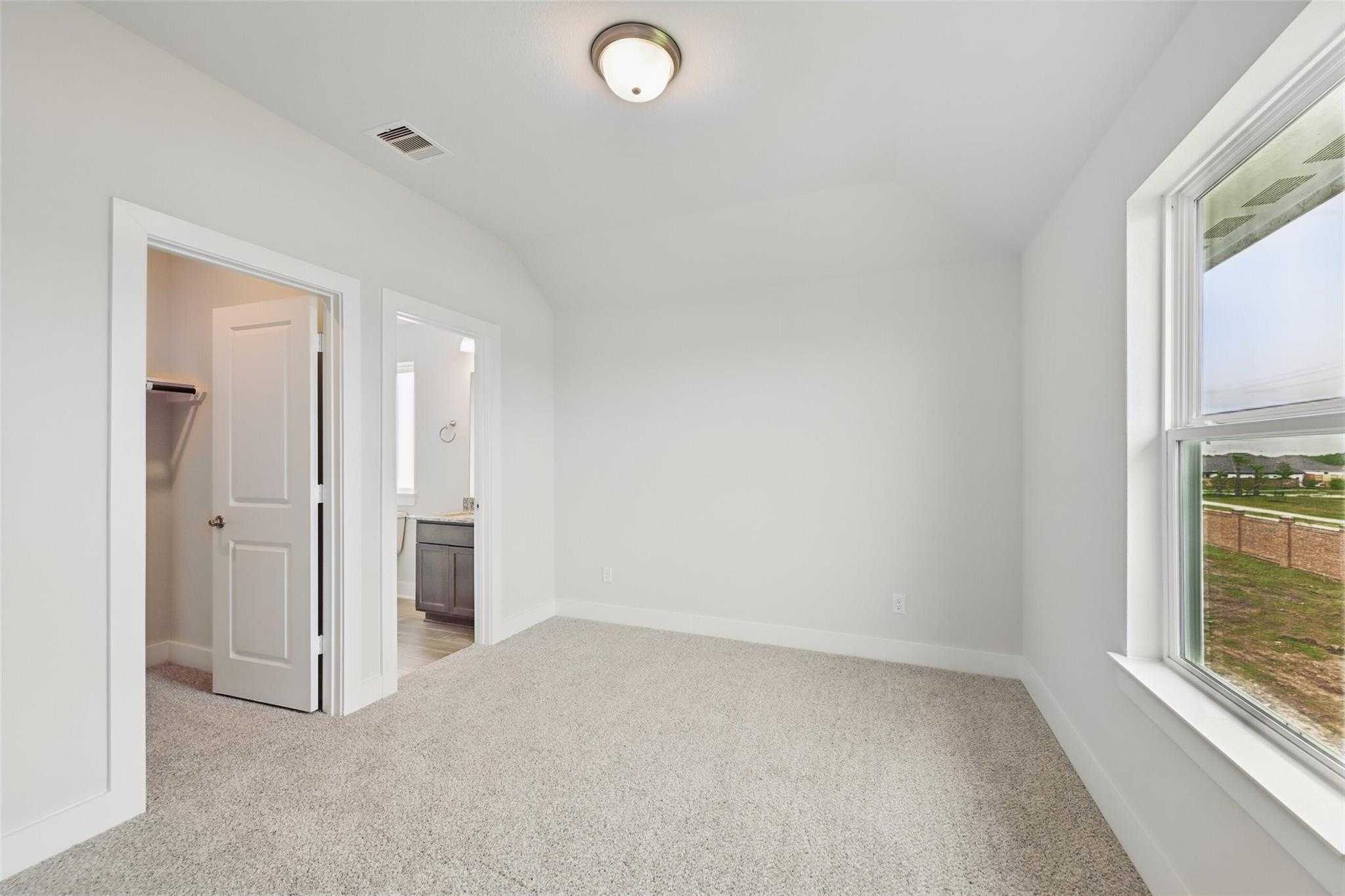 Bright secondary bedroom with en-suite bath, closet, beige carpet, and window view of fields in Davidson Homes The Philip A, Lago Mar Texas
