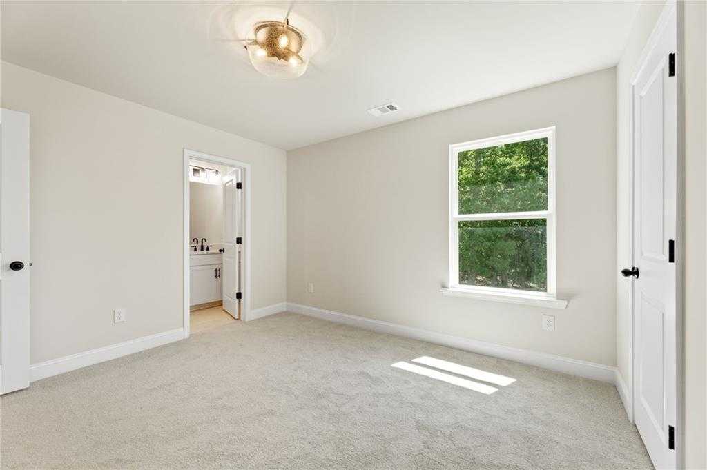 Bright secondary bedroom with beige walls, large window to lush trees, carpet floor, and en-suite bath in Davidson Homes The Hickory E, Buford, GA