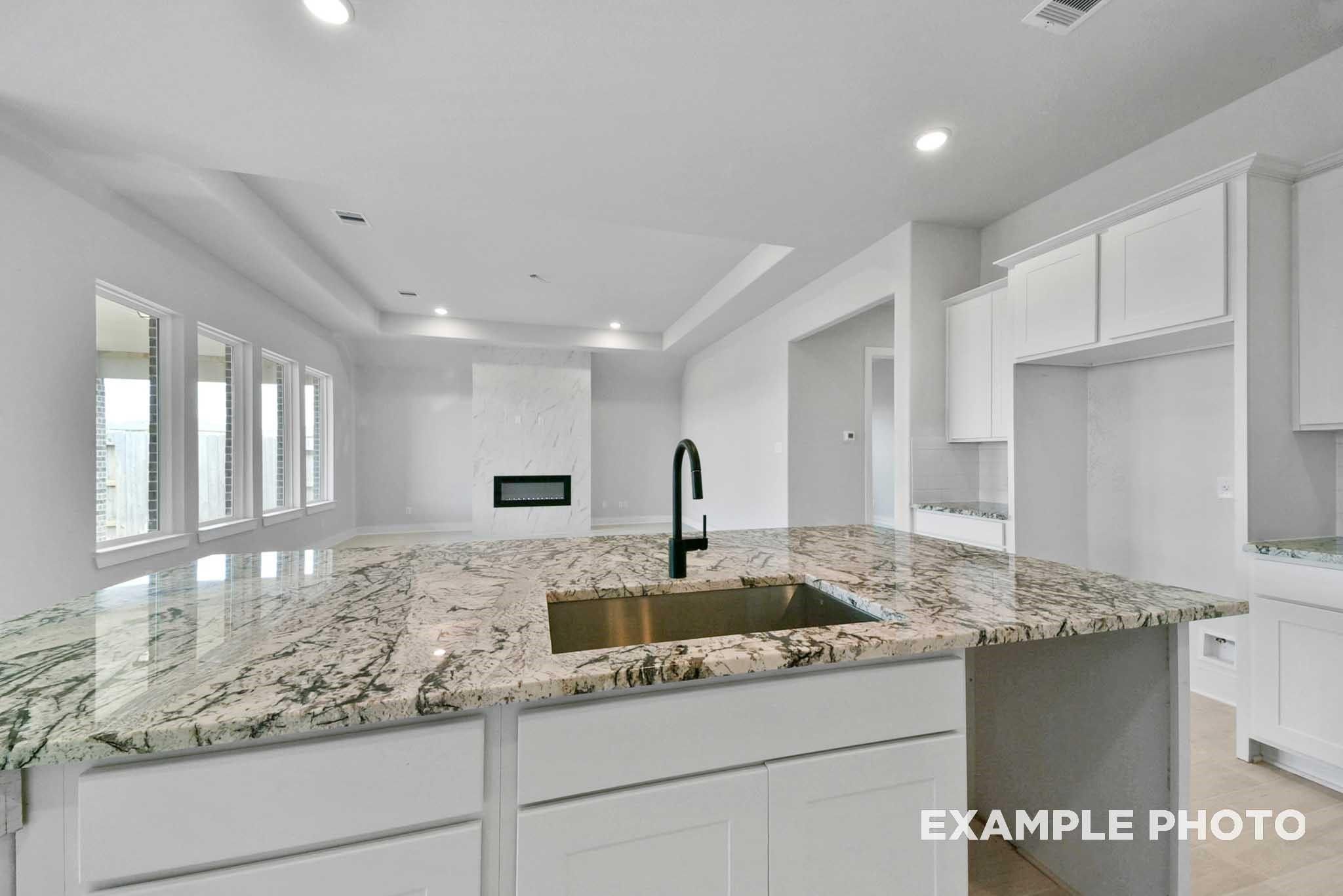 Modern open kitchen with granite island, black faucet, white cabinets in Davidson Homes The George A, Lago Mar, Texas City