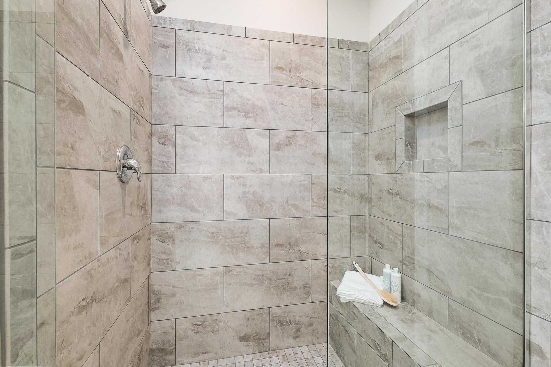 Modern walk-in shower in The Everett C master bath with neutral stone tiles, glass enclosure, niche shelf, and bench