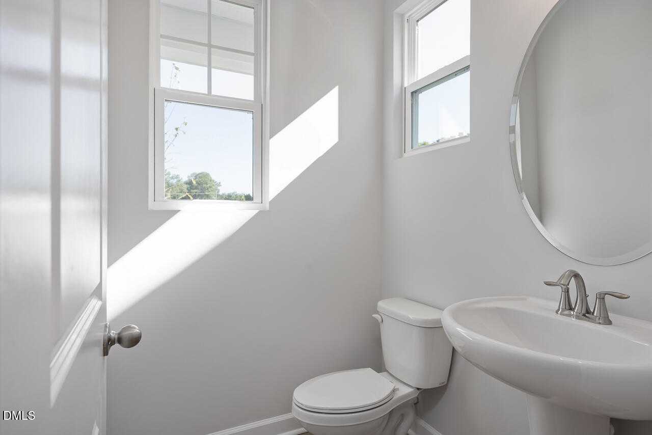 Bright half bath with round mirror, white sink, toilet, and natural light in Davidson Homes The Graham, Fuquay-Varina, NC