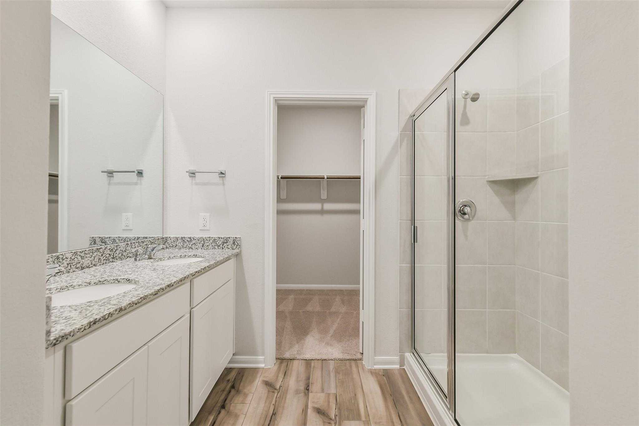 Modern master bathroom featuring double granite vanity, frameless glass shower, and walk-in closet in Davidson Homes The Brazos F, Conroe, Texas