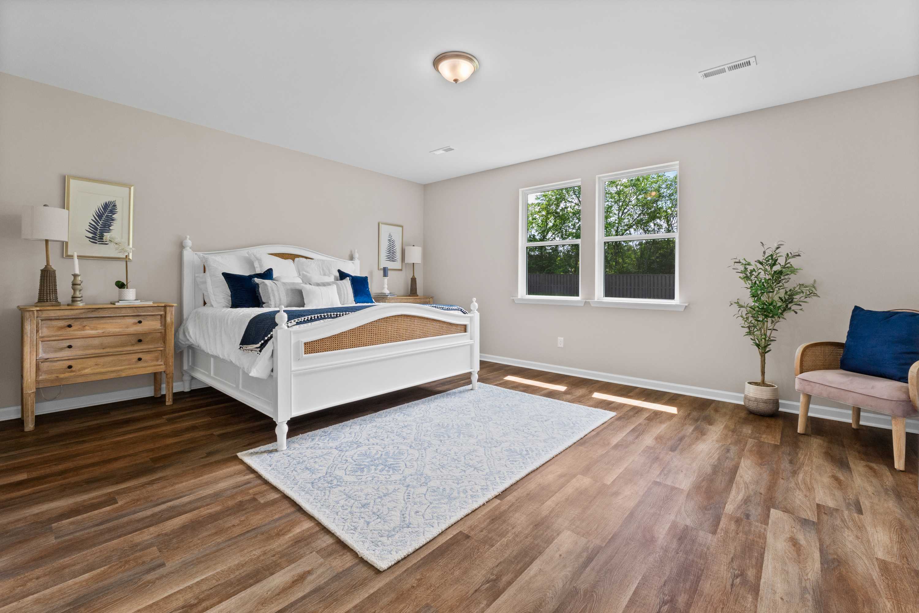 Cozy primary bedroom at Riverton Preserve in Huntsville Alabama with white wooden bed, navy blue pillows, hardwood floors, and large windows
