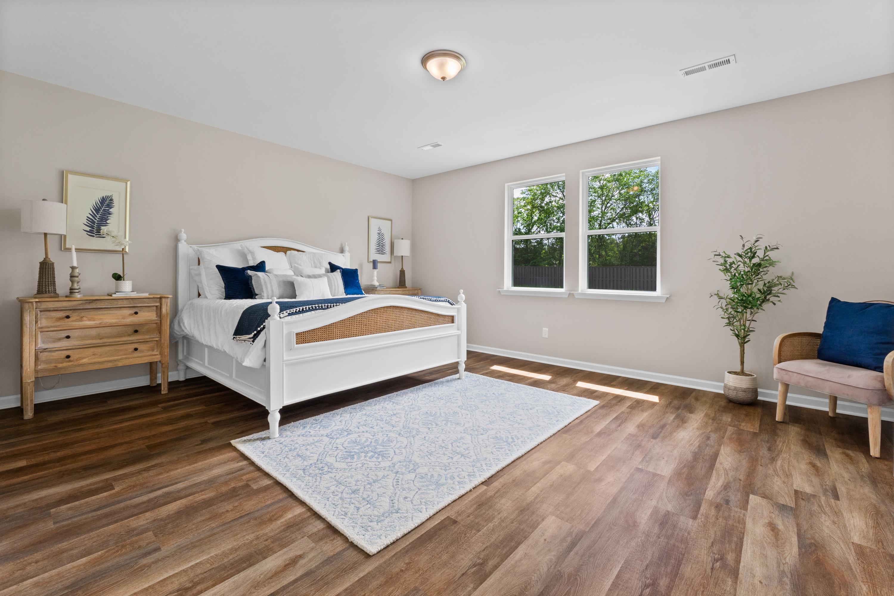 Cozy primary bedroom at Riverton Preserve in Huntsville Alabama with white wooden bed, navy blue pillows, hardwood floors, and large windows
