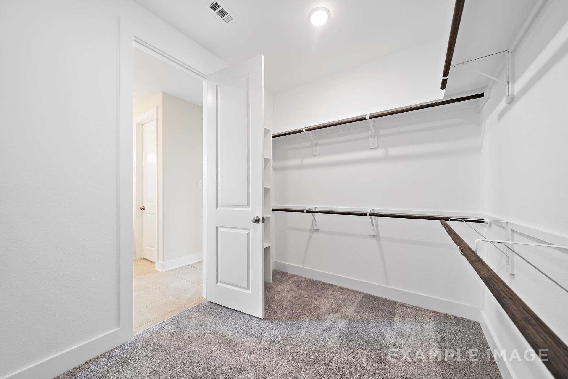 Spacious master walk-in closet in The Diana C by Davidson Homes, with white walls, wooden shelves, hanging rods, and carpeted floor