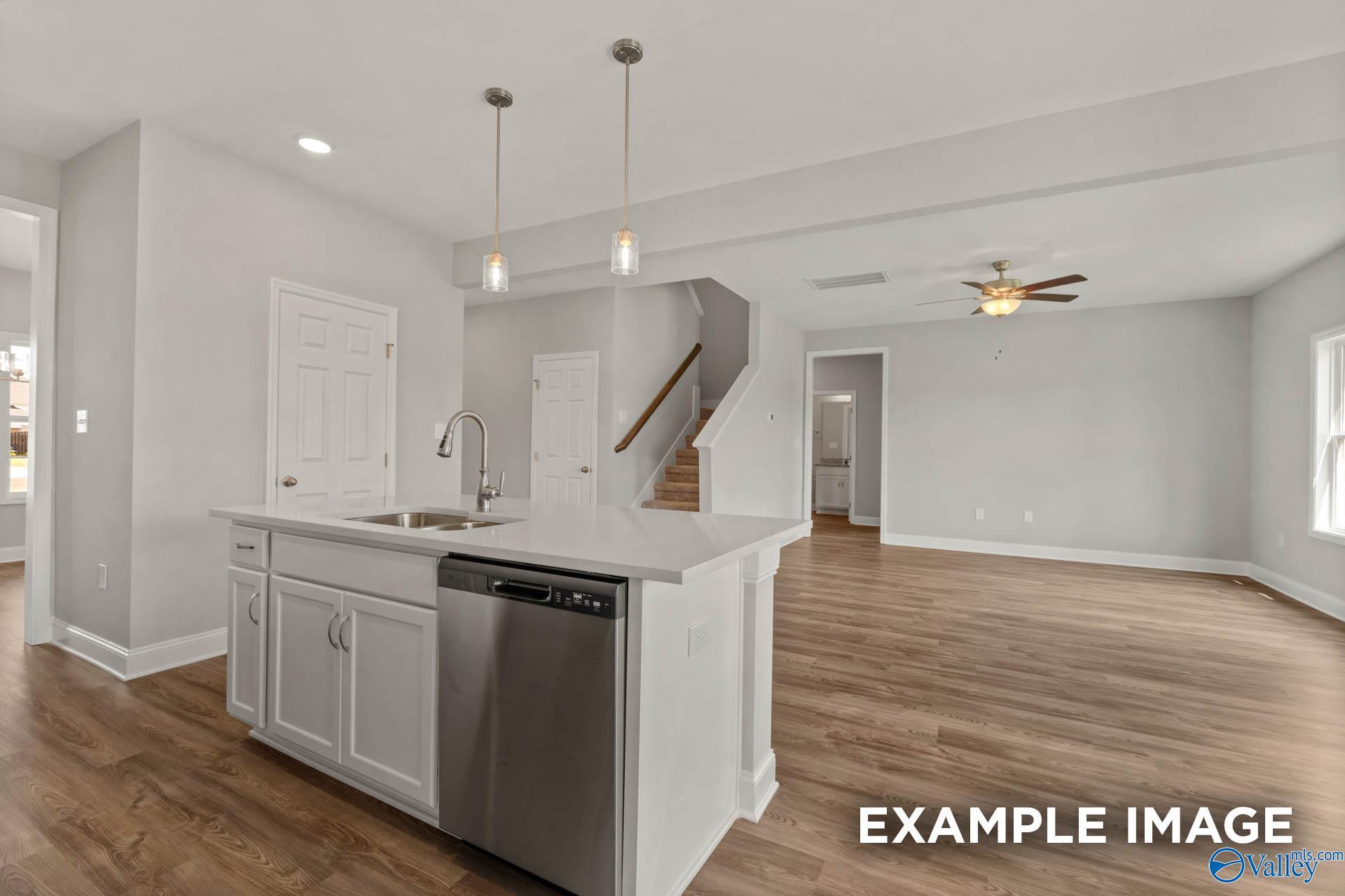 Open-concept kitchen with white island sink, stainless dishwasher, hardwood floors, and staircase in The Shelby B, Heritage Lakes, New Market, Alabama