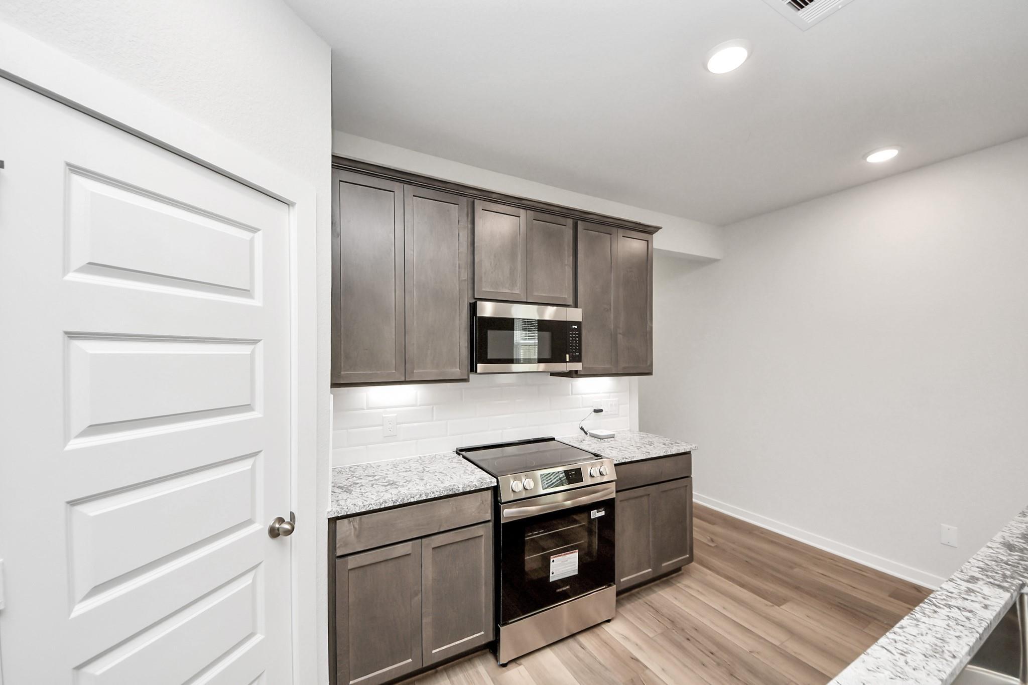 Modern kitchen with gray cabinets, granite countertops, and stainless appliances in The Sabine E home, Liberty Estates.