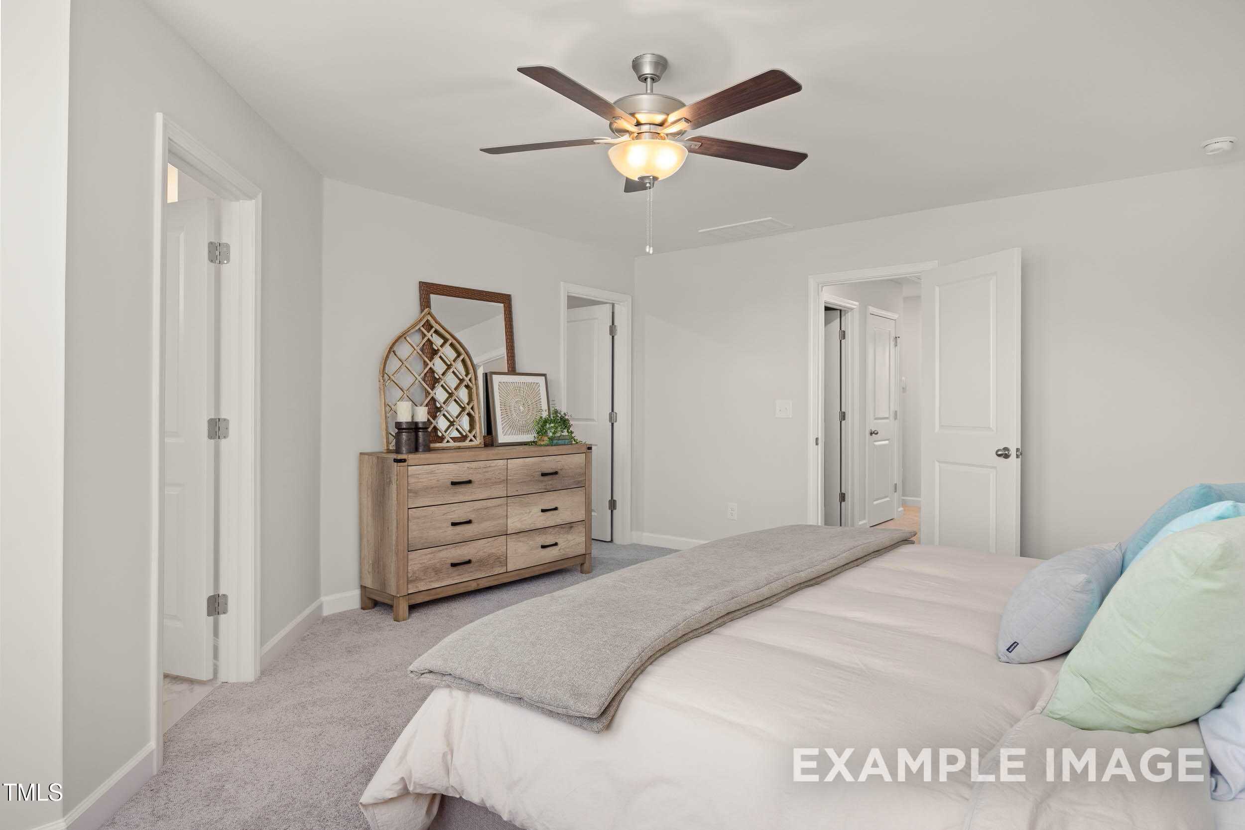 Inviting master bedroom with plush king bed, rustic wooden dresser, and ceiling fan in Davidson Homes The Graham plan, Fuquay-Varina, NC