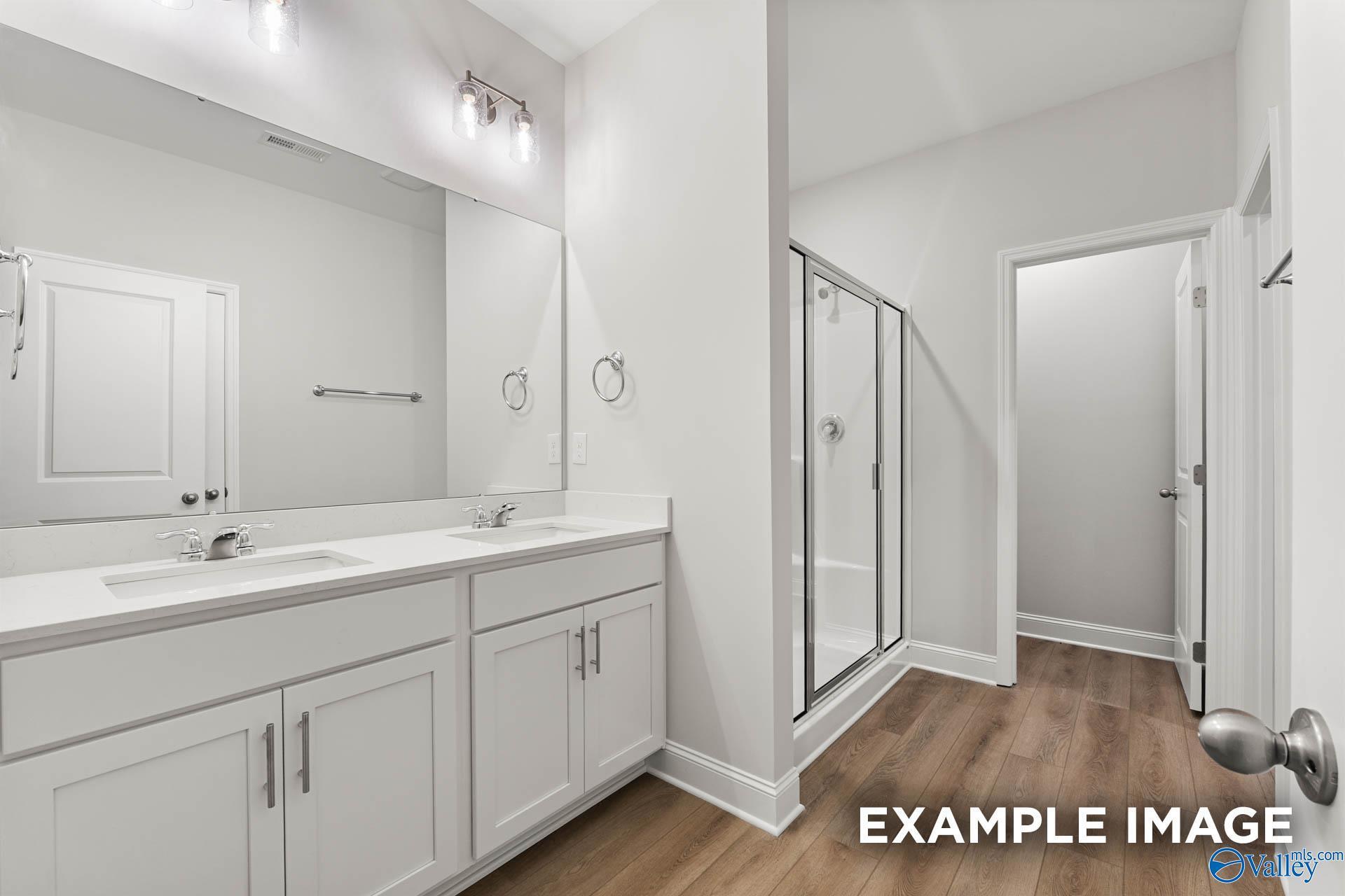 Modern master bathroom featuring double white vanity, large mirror, and glass shower in Davidson Homes The Daphne C, Huntsville, Alabama