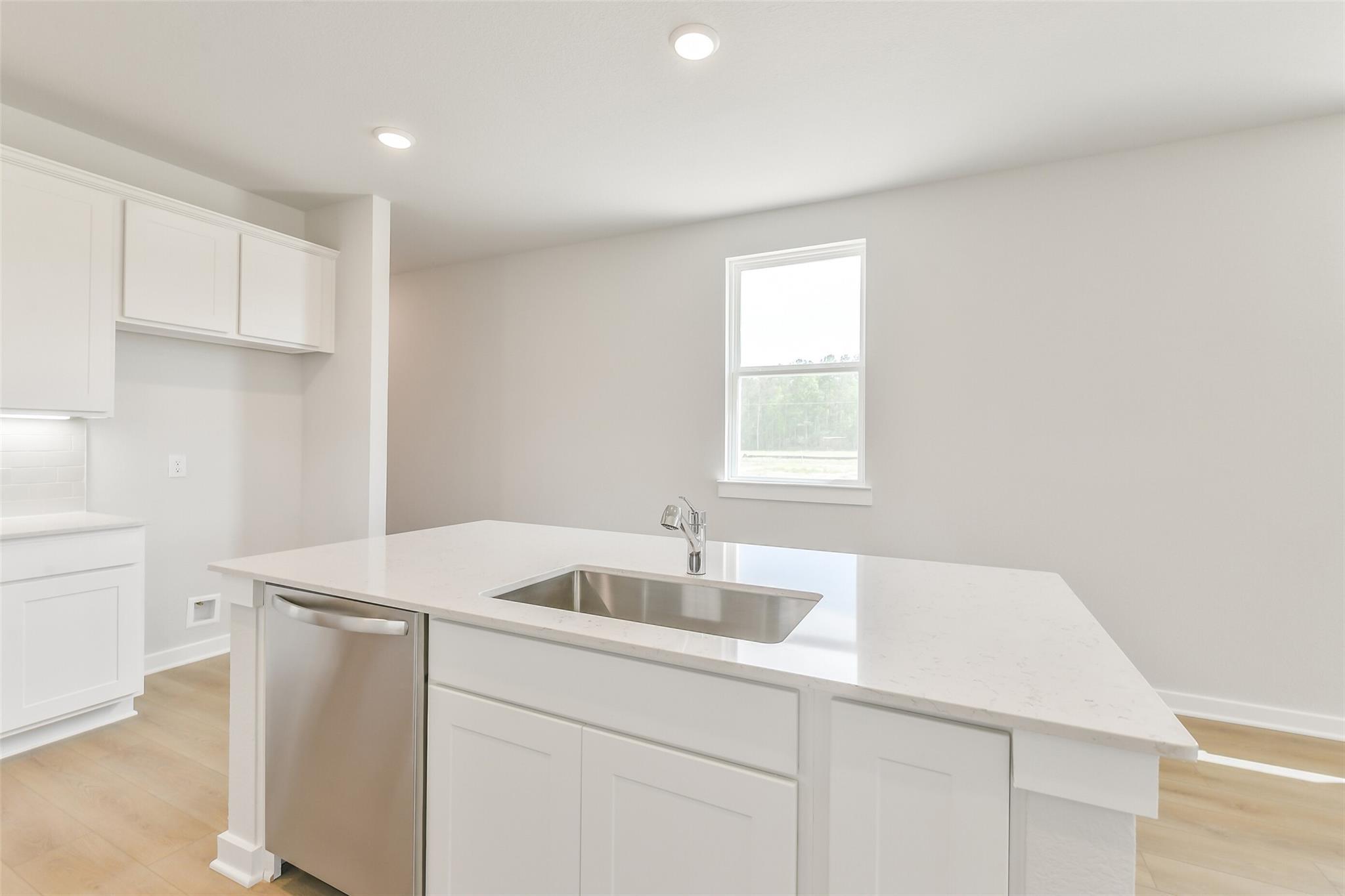 Modern white kitchen island with quartz countertop, stainless sink, faucet, and dishwasher in The Frio G, Conroe Texas