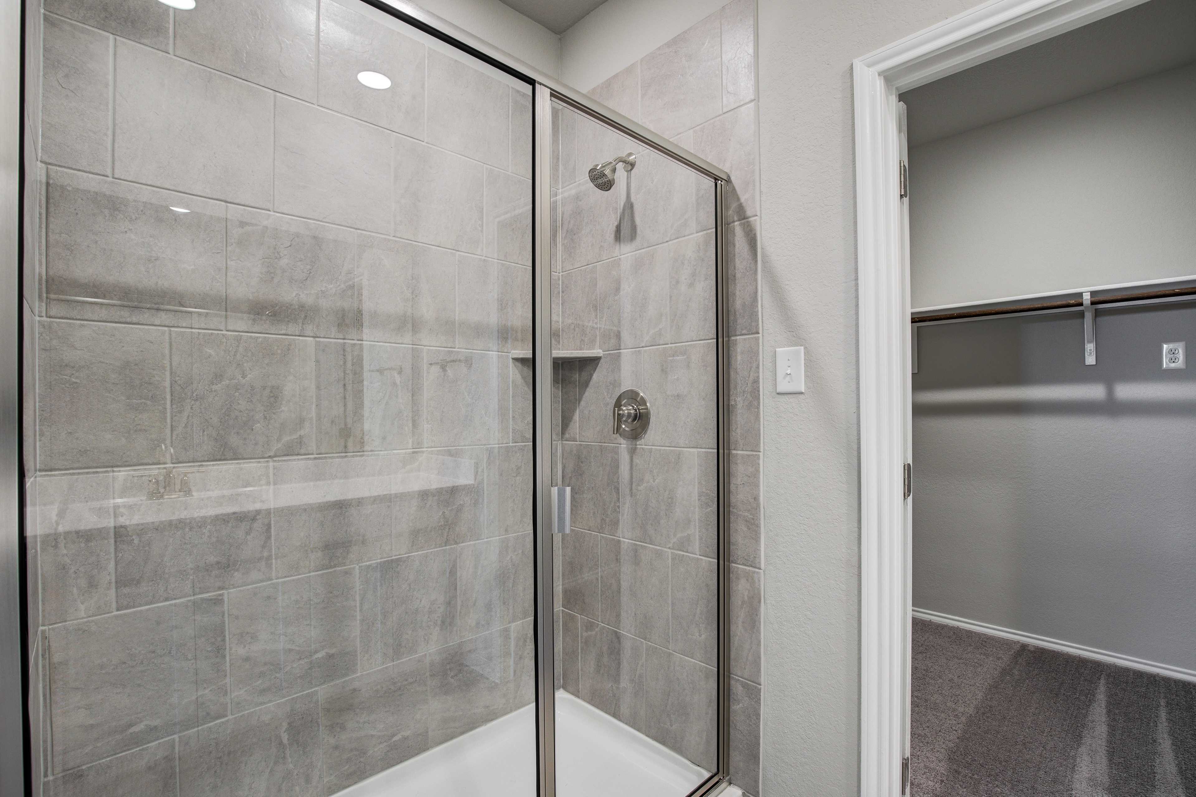 Modern master bathroom in The Blanco B featuring frameless glass walk-in shower, gray subway tile, niche shelf, and closet doorway