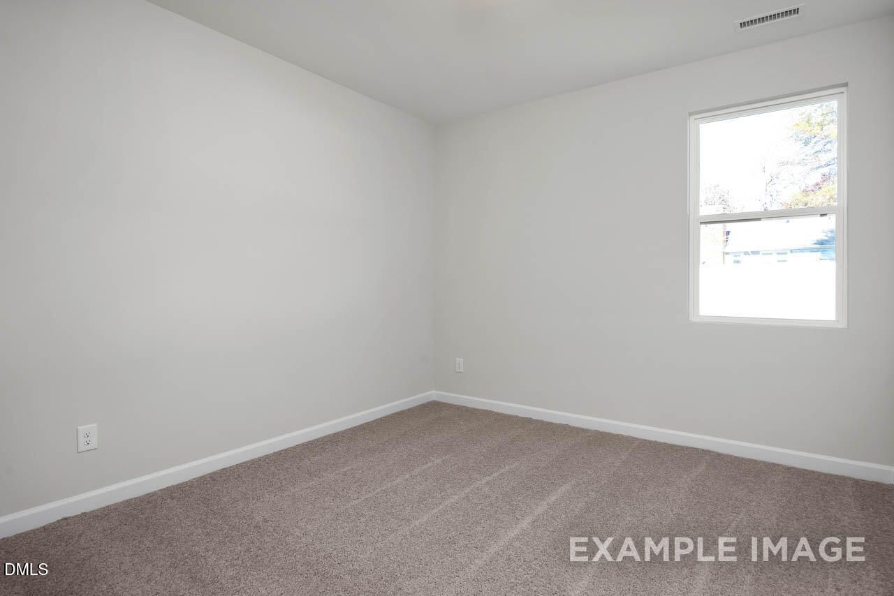 Bright empty bedroom with white walls, beige carpet, and large window in Davidson Homes The Adalynn A, Lillington, NC