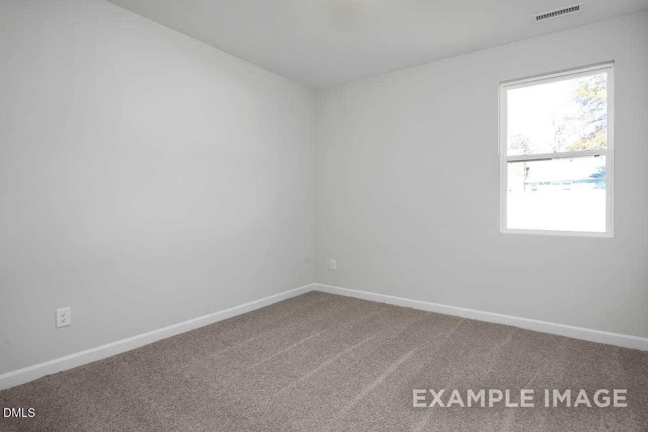 Bright empty bedroom with white walls, beige carpet, and large window in Davidson Homes The Adalynn A, Lillington, NC