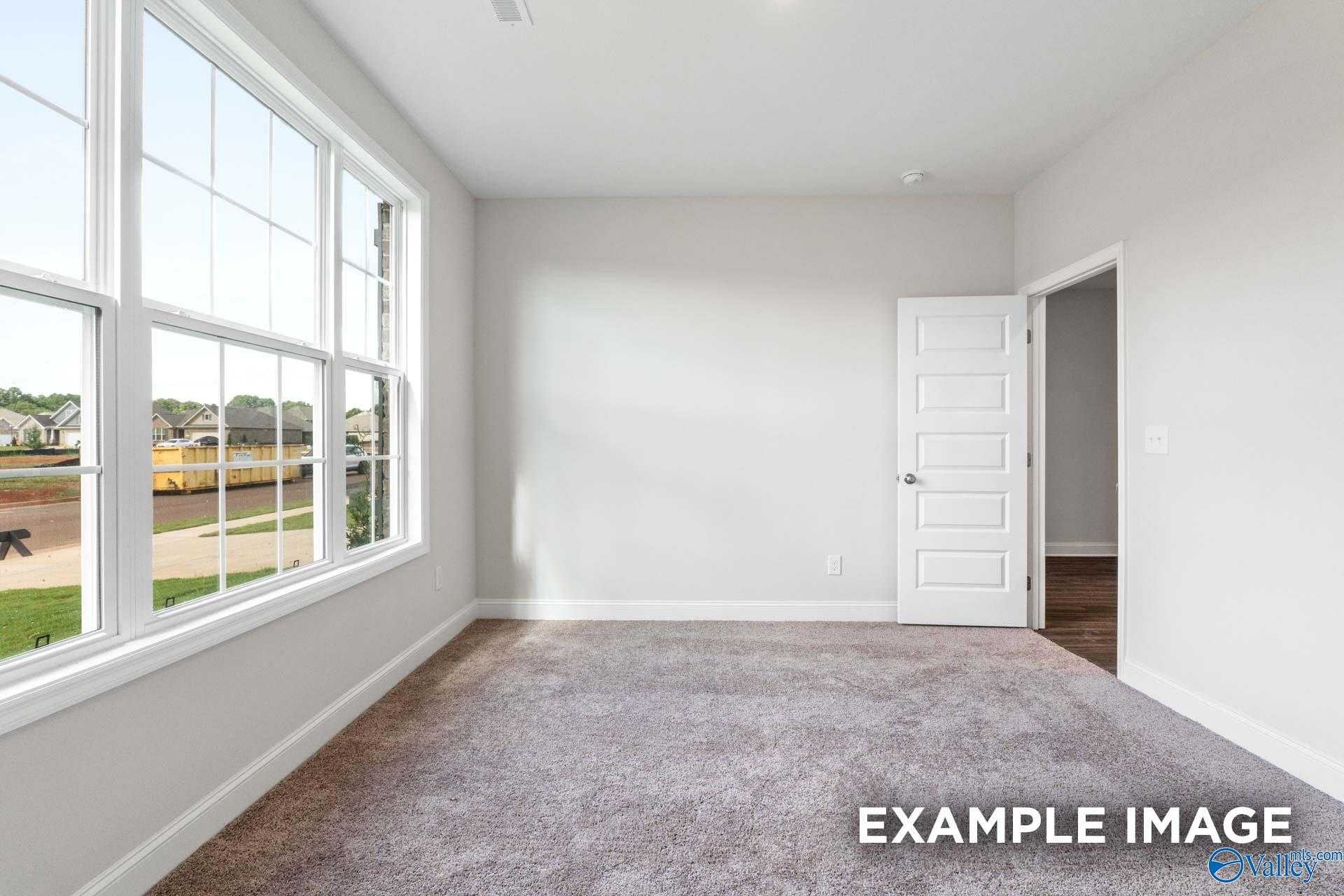 Bright living room with large windows, gray carpet, and neighborhood view in The Montgomery floor plan, Athens, Alabama