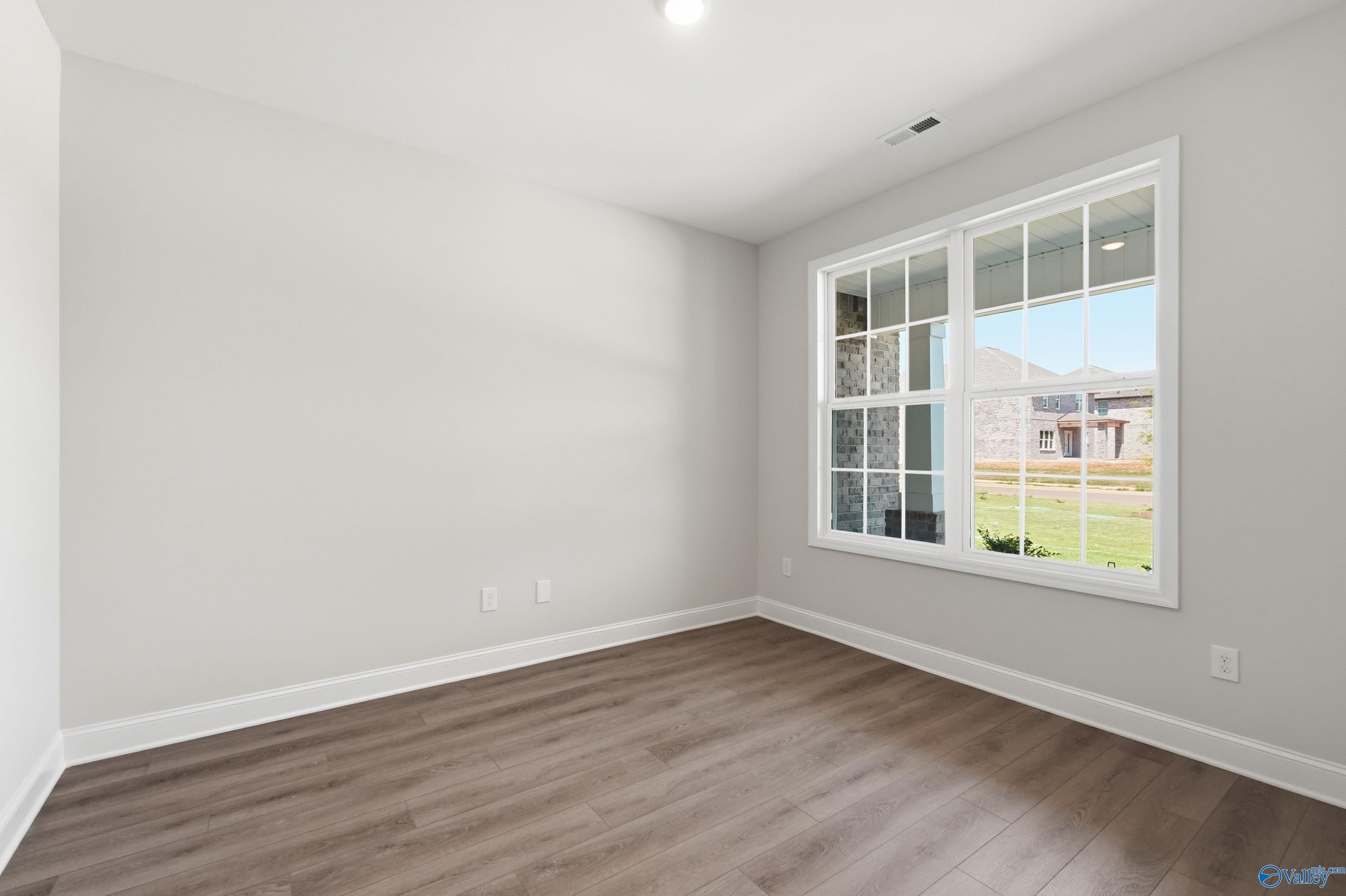 Bright empty bedroom with light gray walls, hardwood floors, and large window overlooking green field in The Rockford B, Athens, Alabama