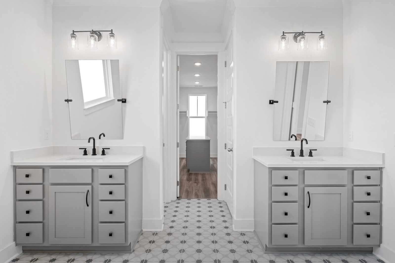 Elegant double vanity bathroom with gray cabinets, patterned tile floor, and walk-in closet view in Davidson Homes The Alston A, Murfreesboro