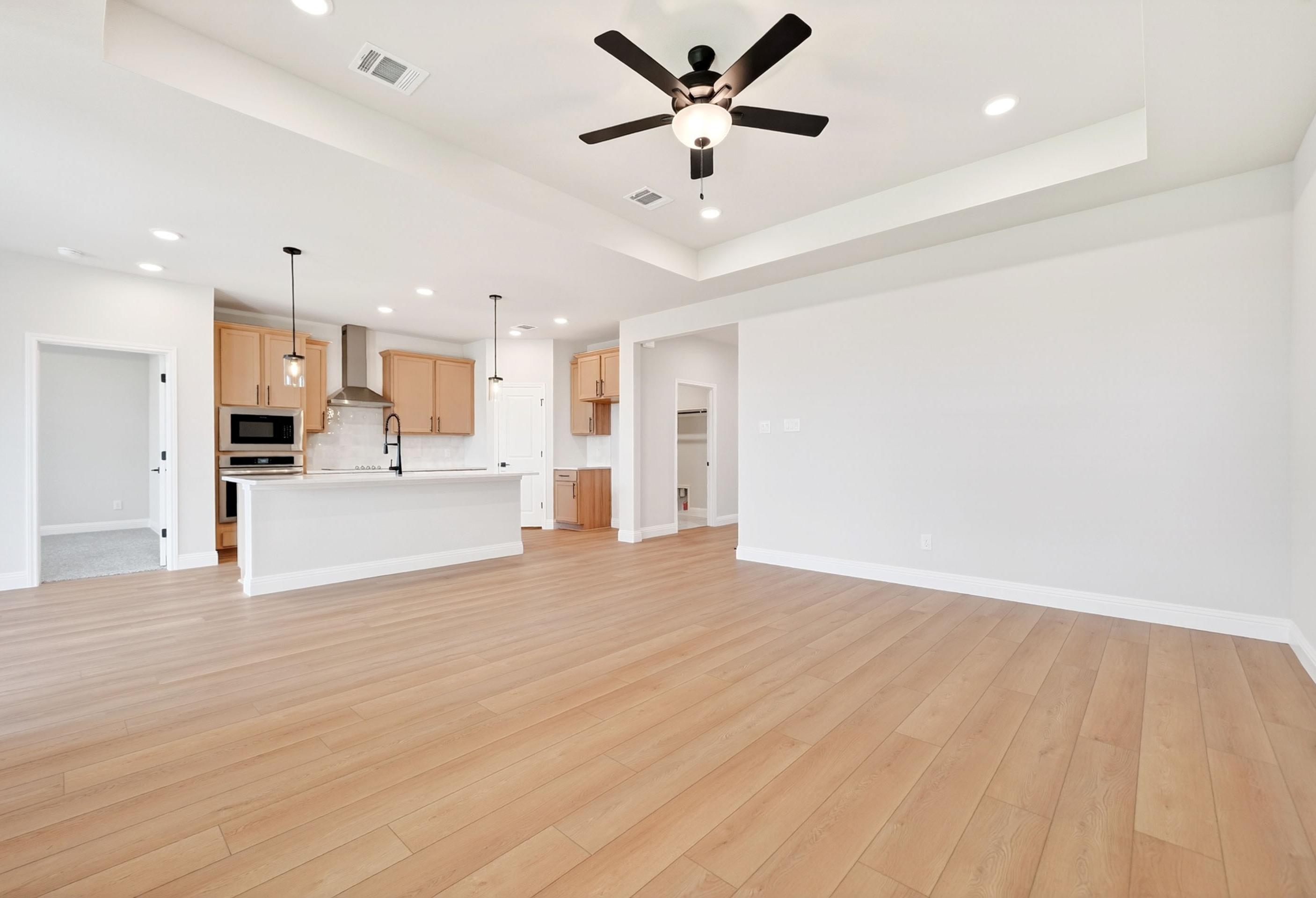 Open-concept living room and kitchen in The Holly by Davidson Homes featuring light wood flooring and tray ceiling.