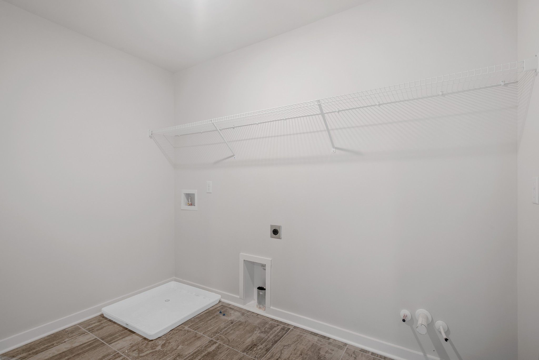 Laundry room with wire shelving, tile flooring, and washer hookups in The Willow B floor plan at Calista Farms.