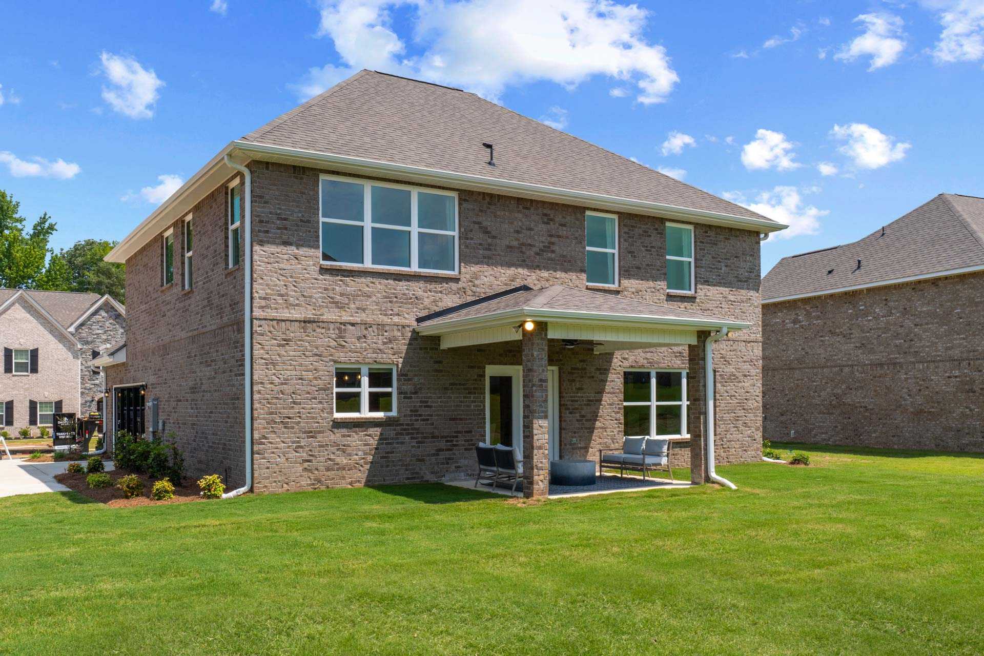 Brick two-story home exterior at Creek Grove in New Market, Alabama with covered side porch, seating, and manicured lawn