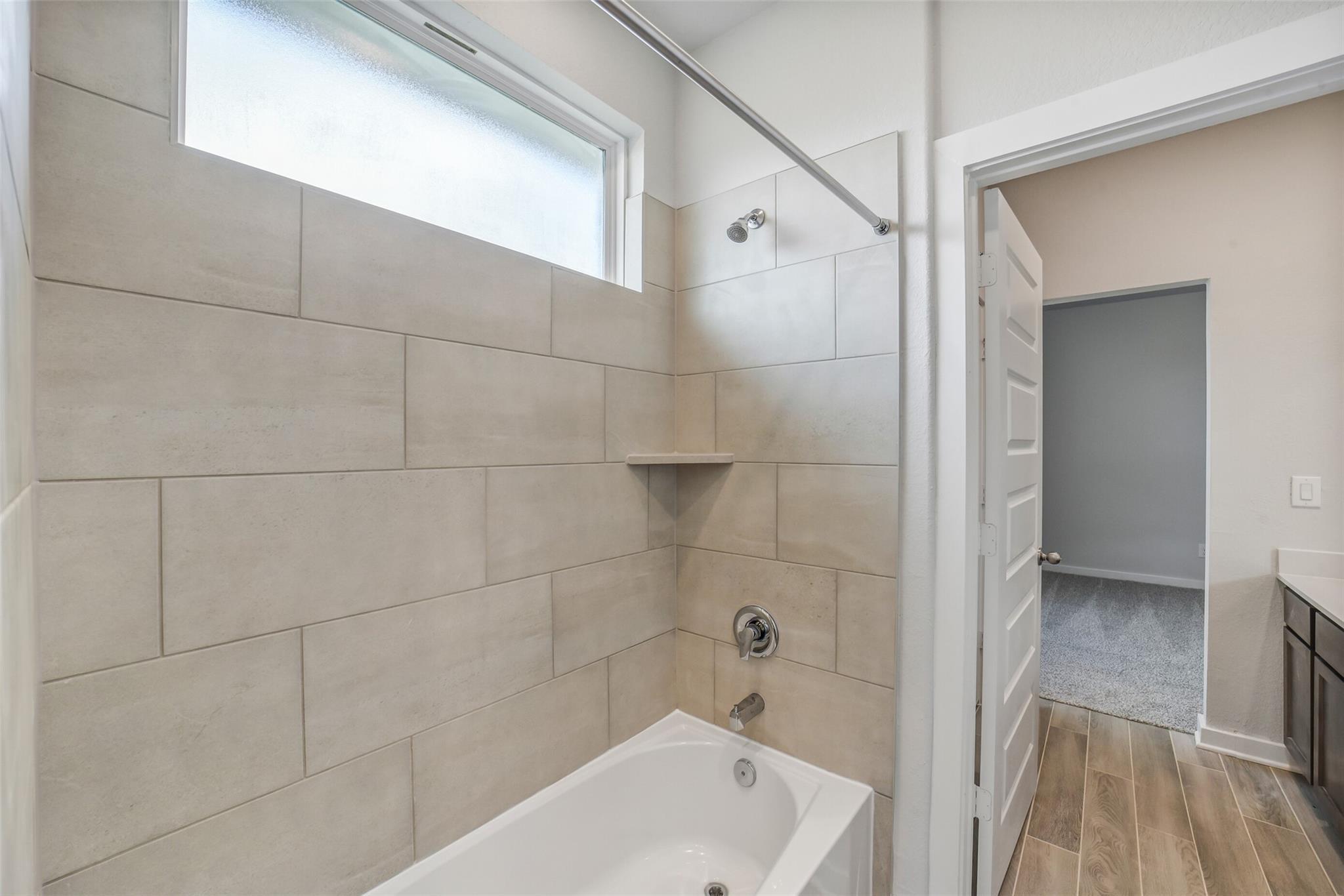 Modern beige-tiled bathroom with bathtub shower combo, frosted window, and adjacent vanity in Davidson Homes The Acadia C, Magnolia Texas