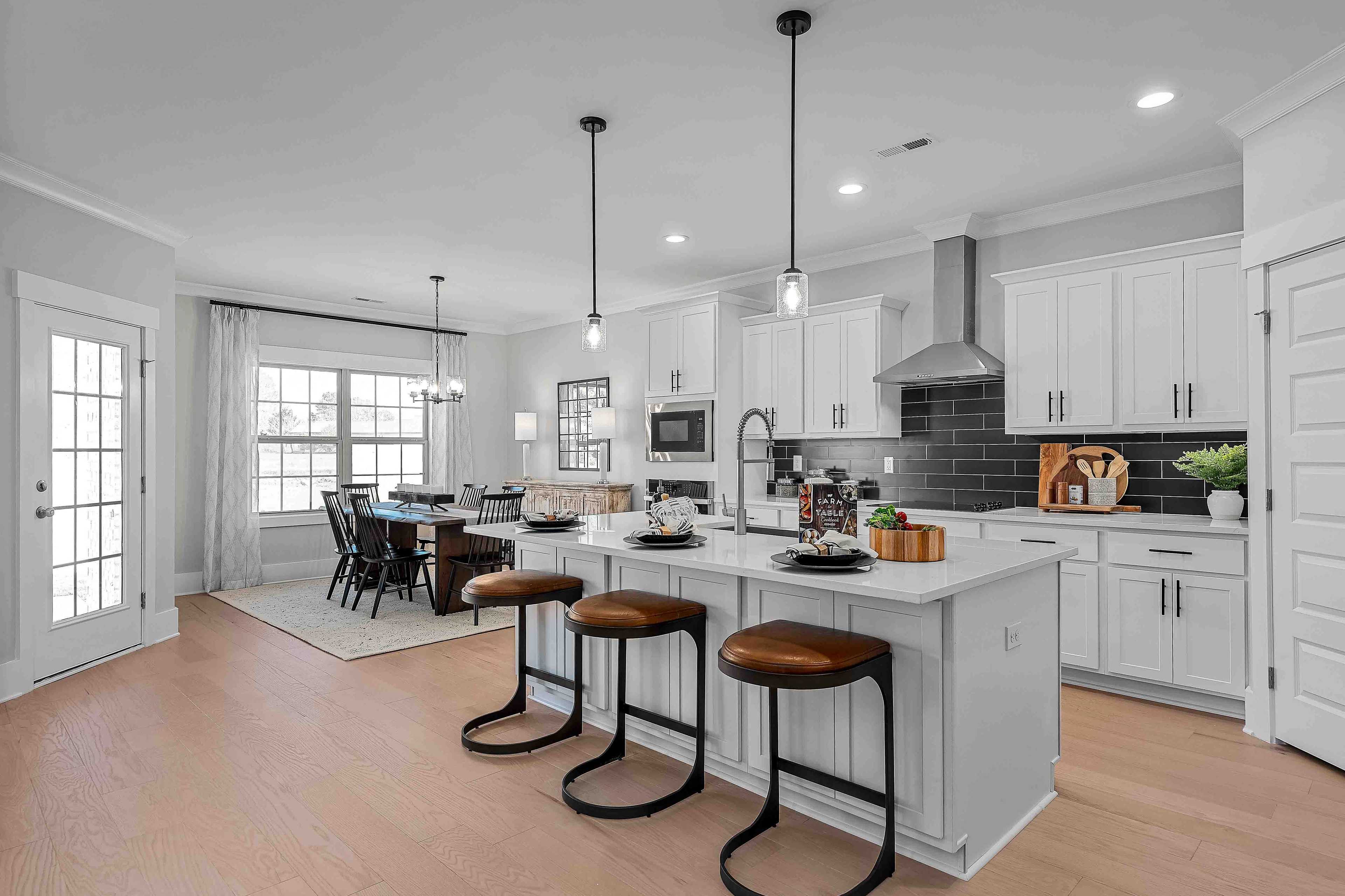 Open-concept kitchen at Cain Park in Hartselle Alabama with white cabinets, black island seating, hardwood floors, and dining area