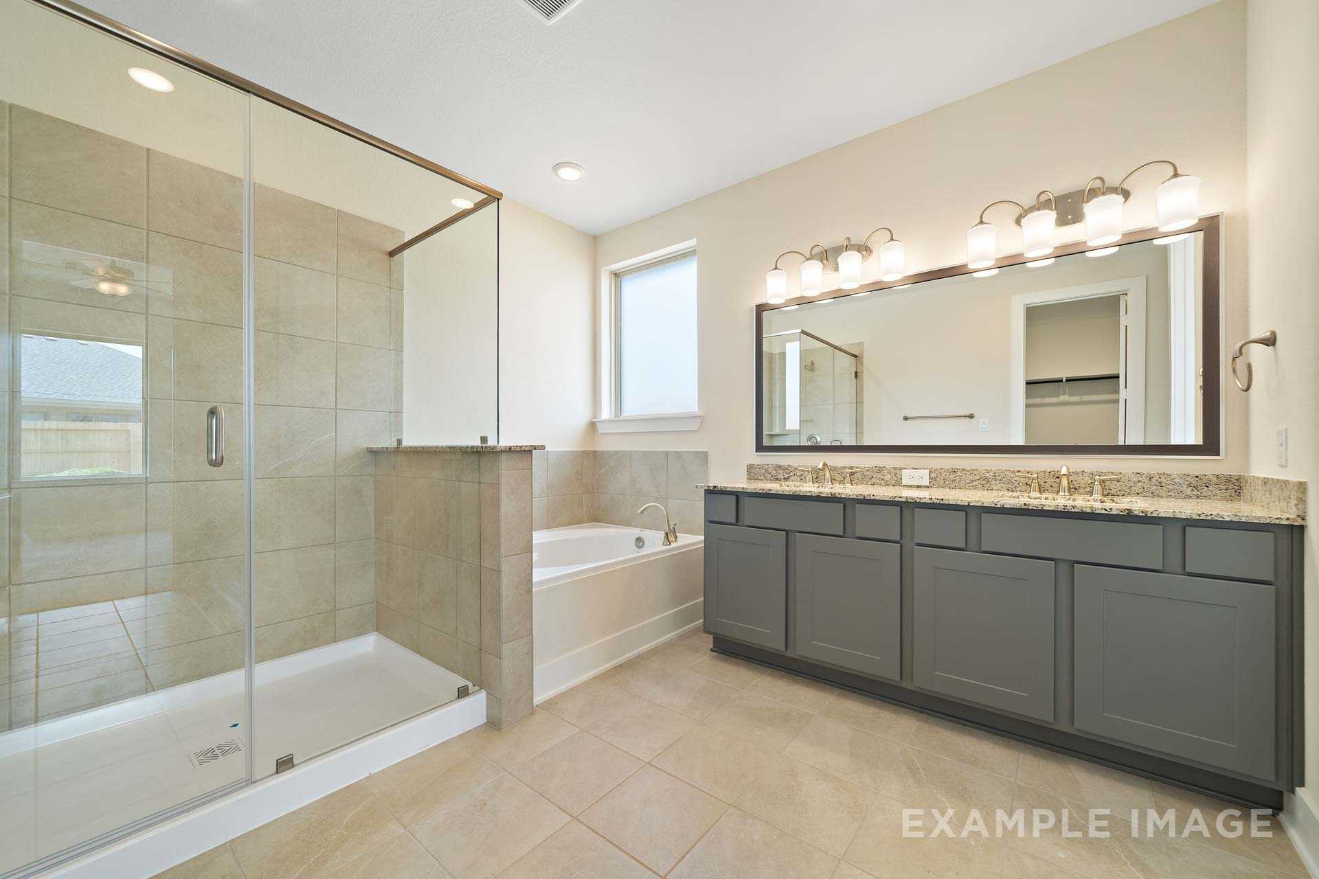 Spacious master bathroom in The Diana C featuring frameless glass shower, soaking tub, and double vanity with dark cabinets