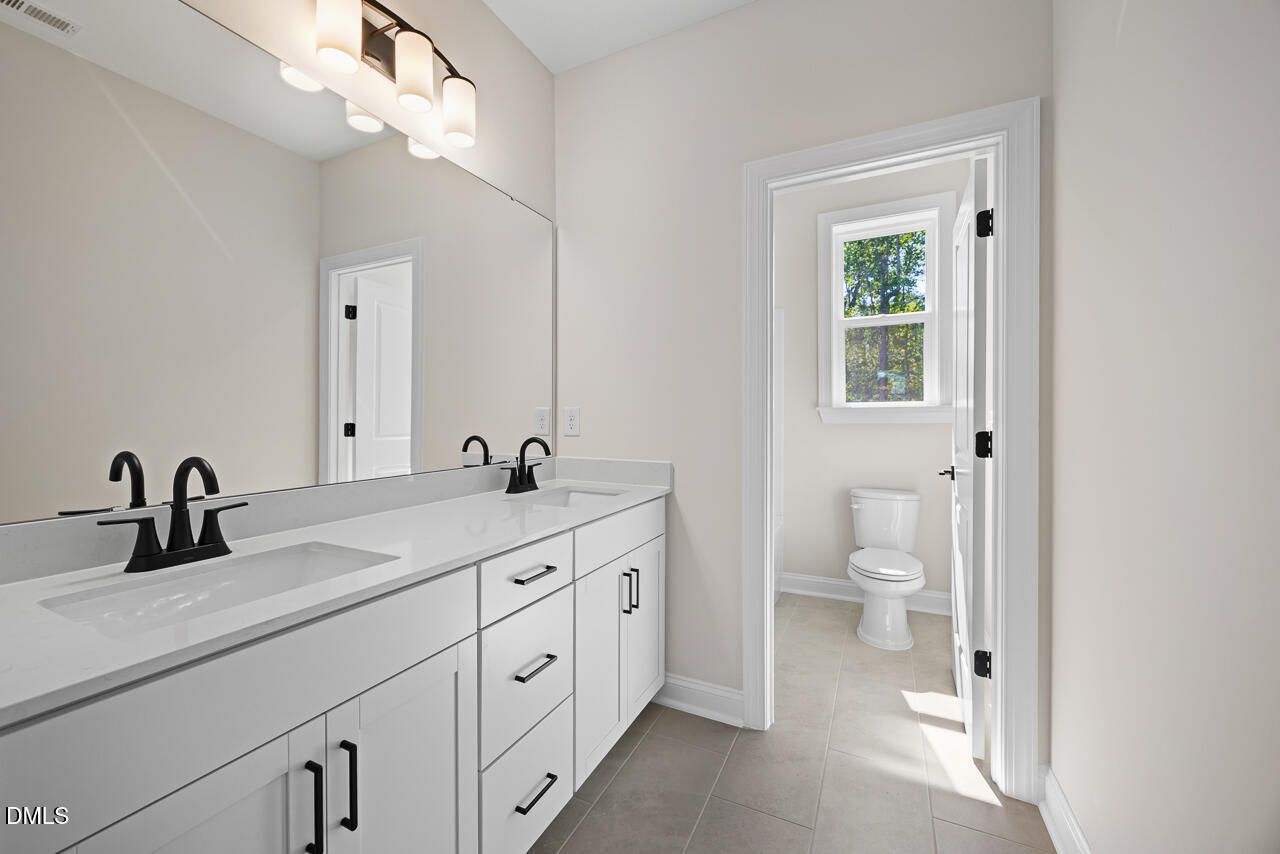 Double vanity bathroom with white cabinets, black faucets, and separate toilet room in Davidson Homes Crawford D, Wake Forest, NC
