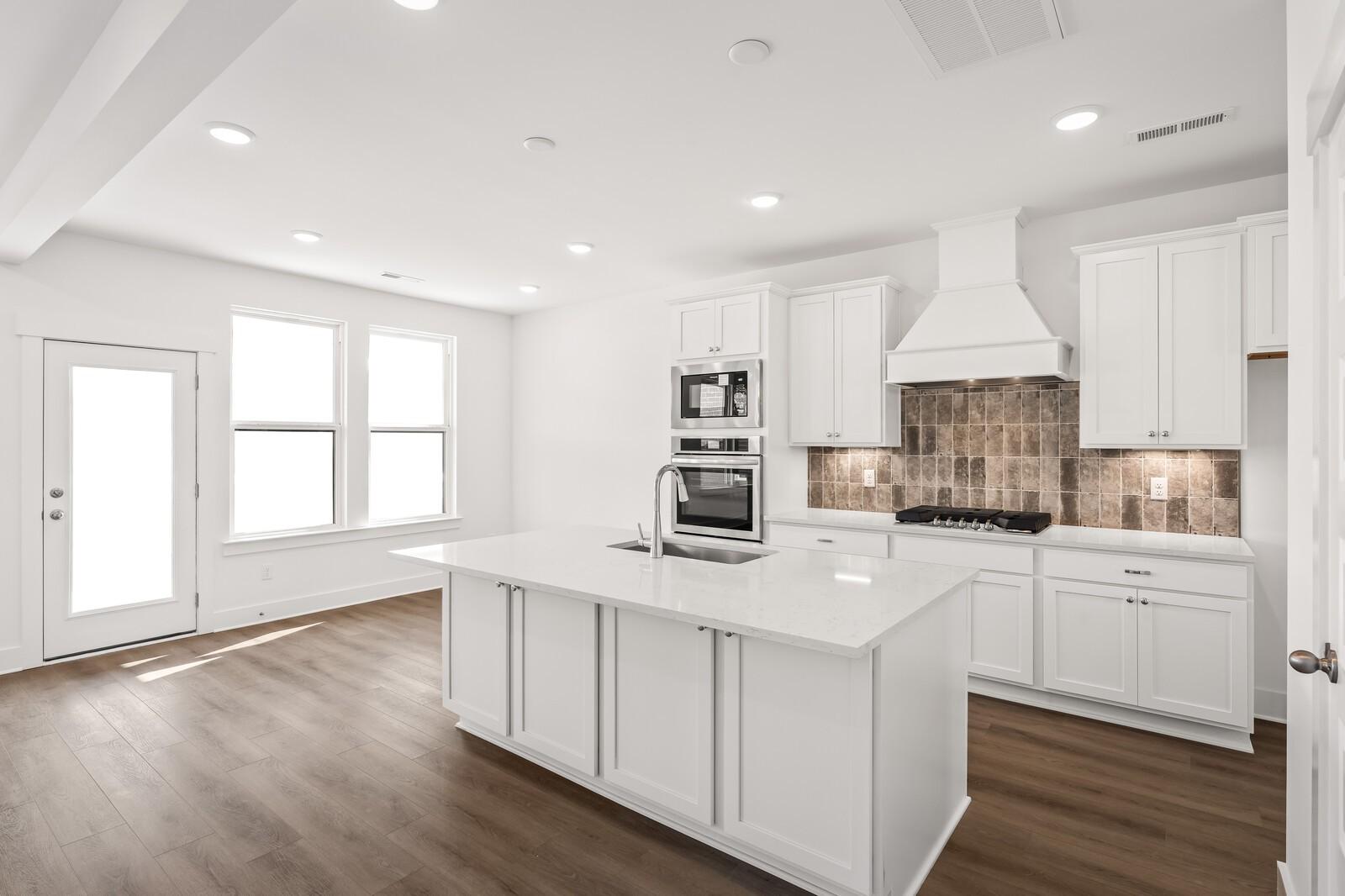 Modern open-concept kitchen with white cabinets, large island sink, double oven, and brick backsplash in Davidson Homes The Willow D, Mt. Juliet