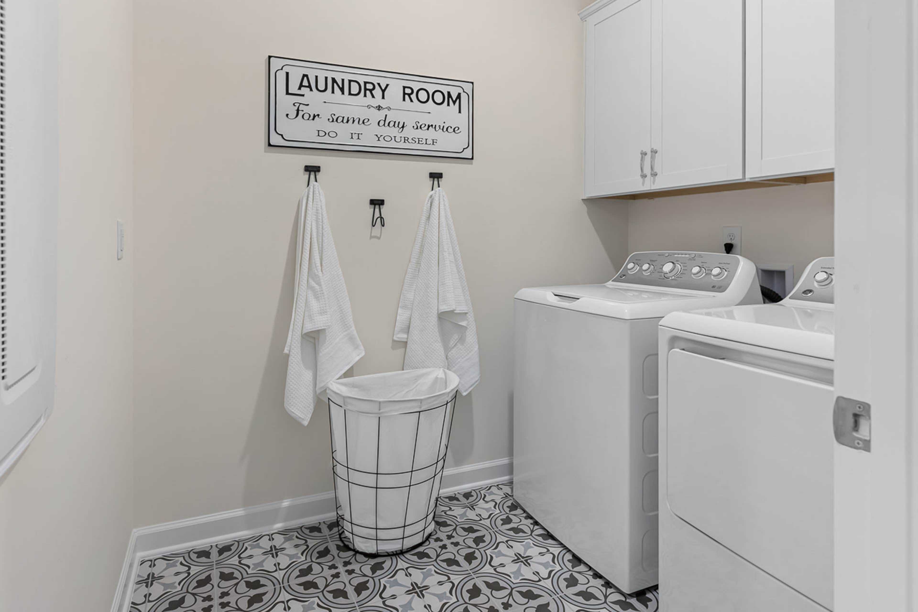 Spacious laundry room in Weatherford East, Angier NC with white washer dryer, hanging towels, woven basket, and patterned tile floor by Davidson Homes