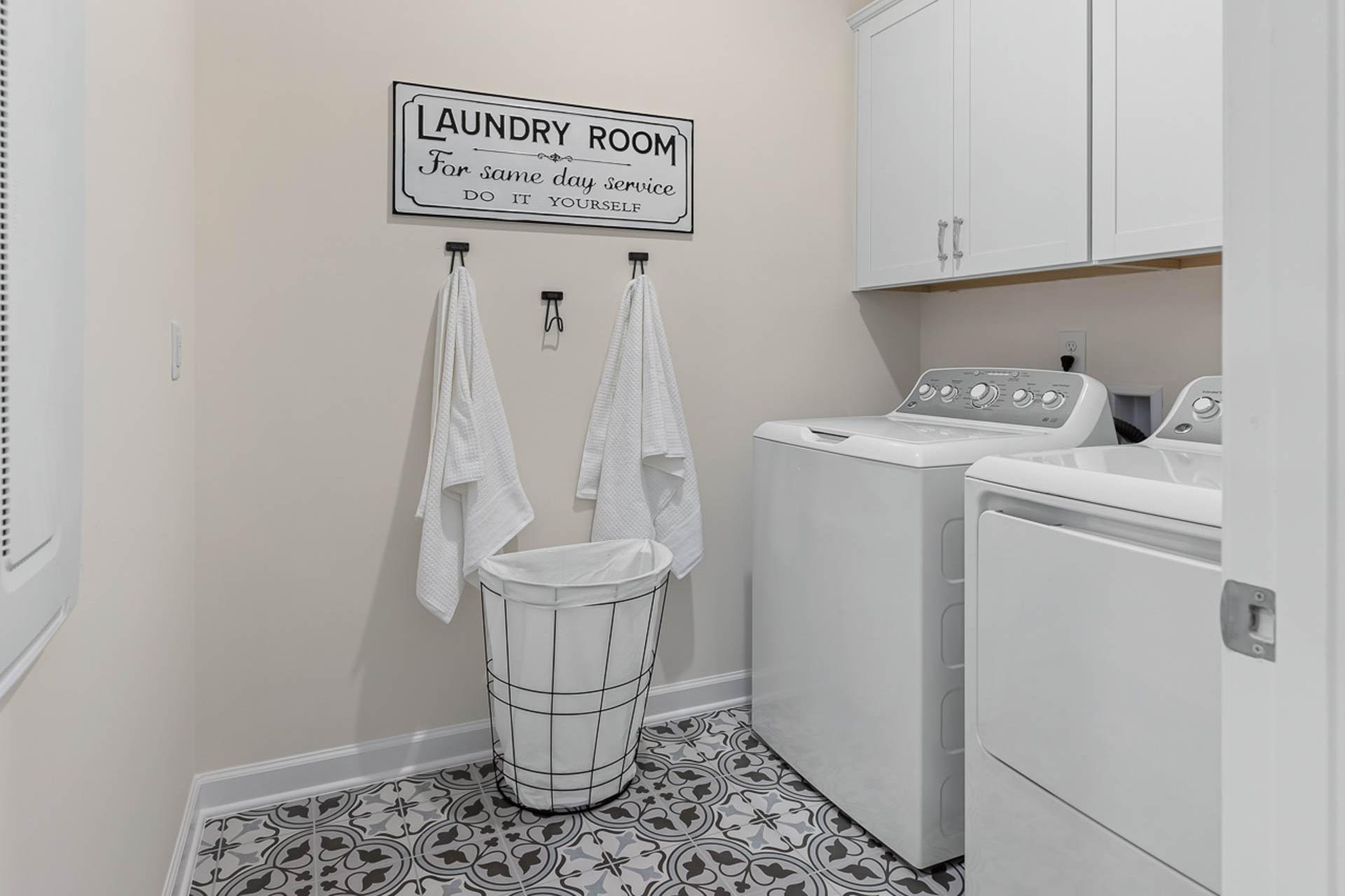 Spacious laundry room in Weatherford East, Angier NC with white washer dryer, hanging towels, woven basket, and patterned tile floor by Davidson Homes