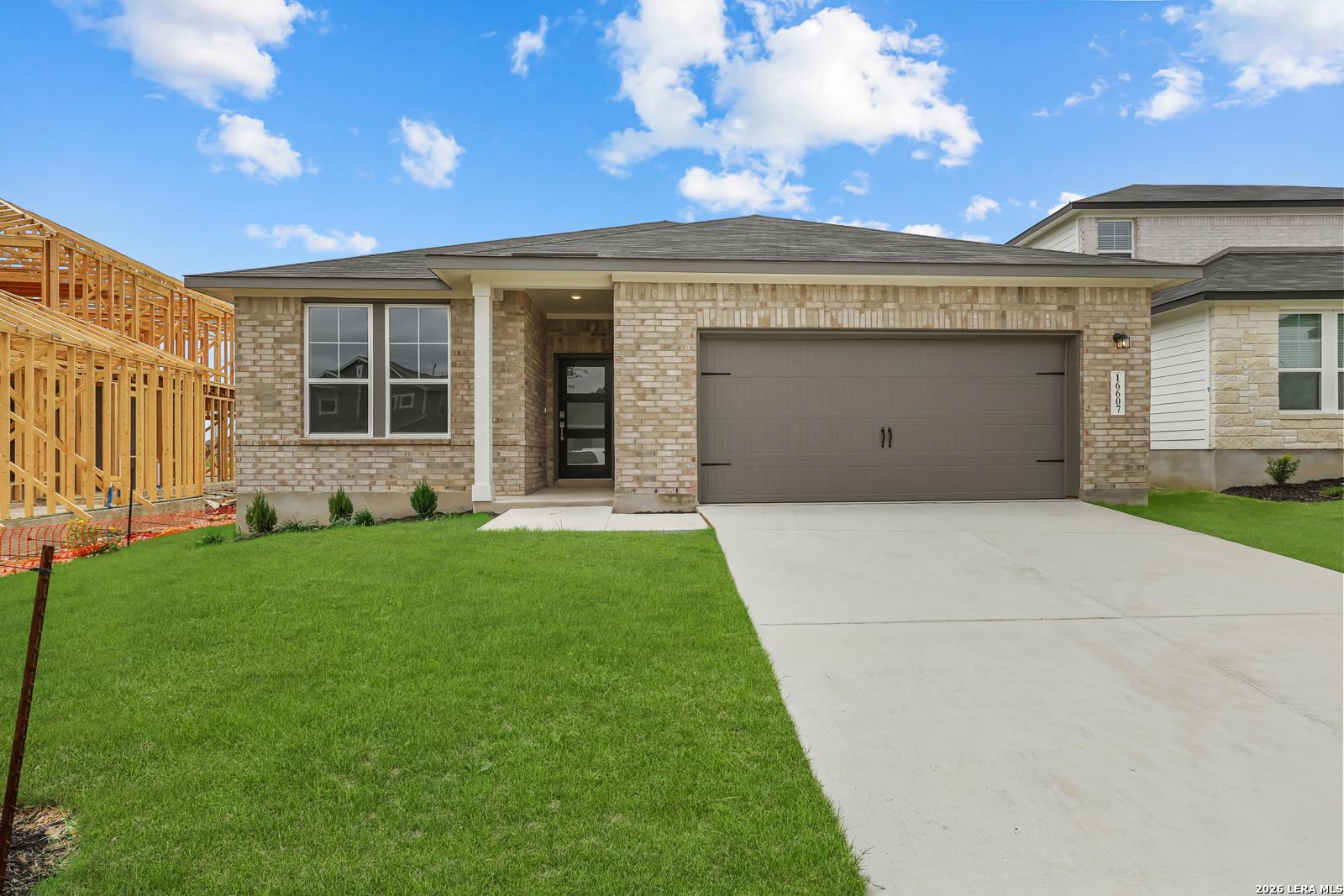 Modern brick single-story home with 2-car garage, front porch, and lush green lawn in Hickory Ridge, Elmendorf, Texas - Davidson Homes Glenwood E