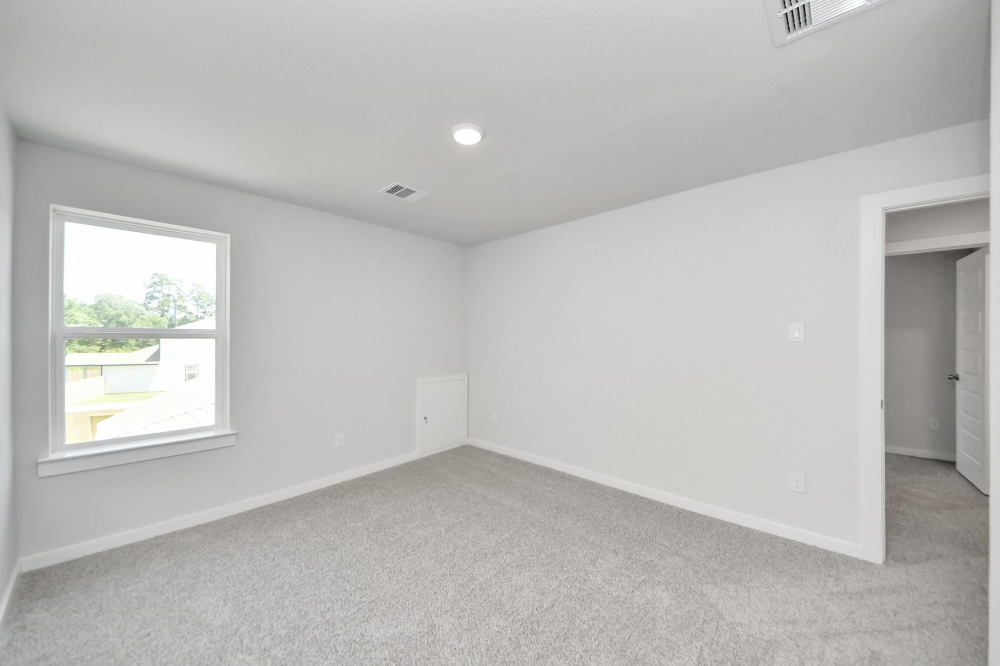 Spacious carpeted bedroom with white walls in The Sabine F floor plan at Liberty Estates, Cleveland, Texas.