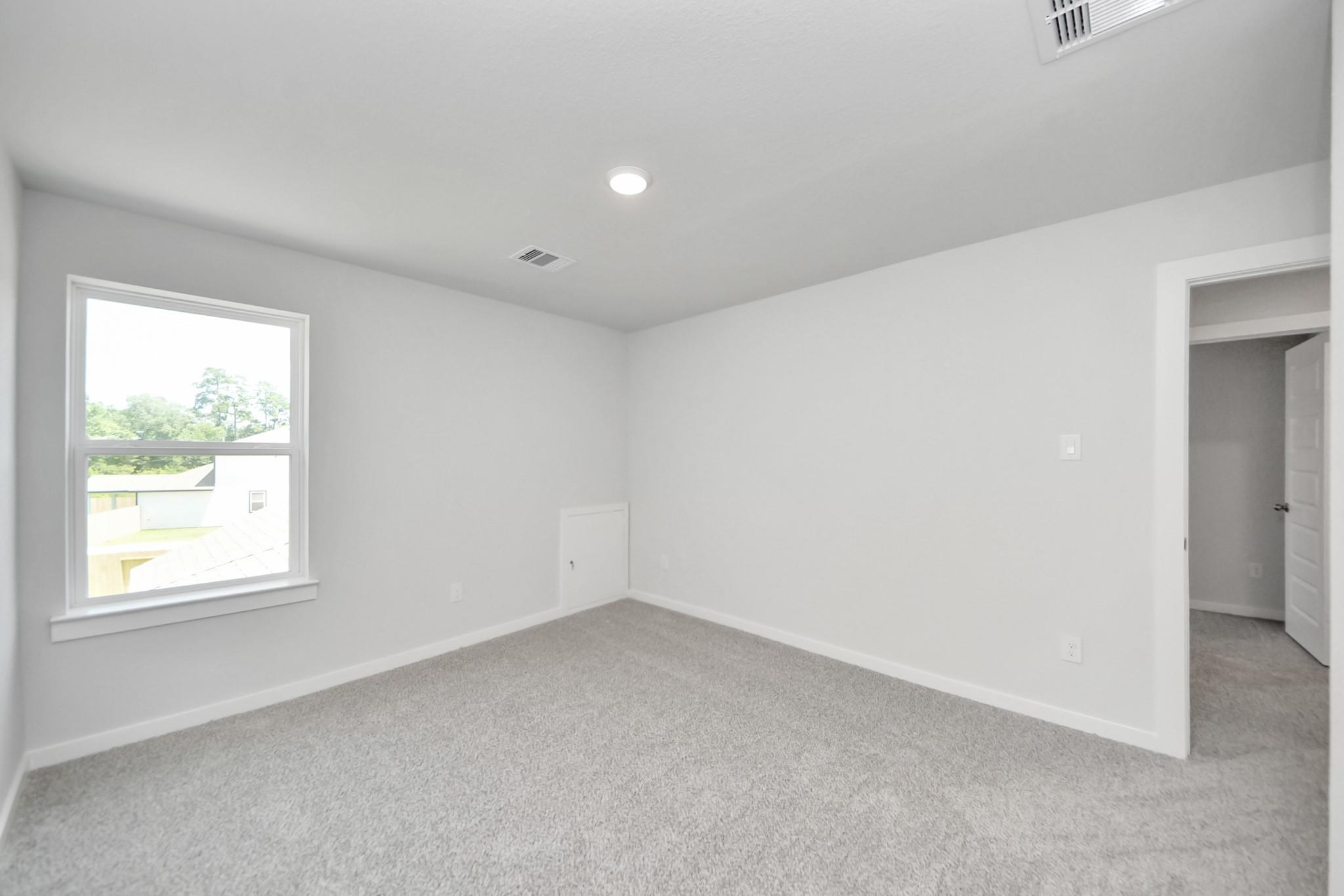 Spacious carpeted bedroom with white walls in The Sabine F floor plan at Liberty Estates, Cleveland, Texas.