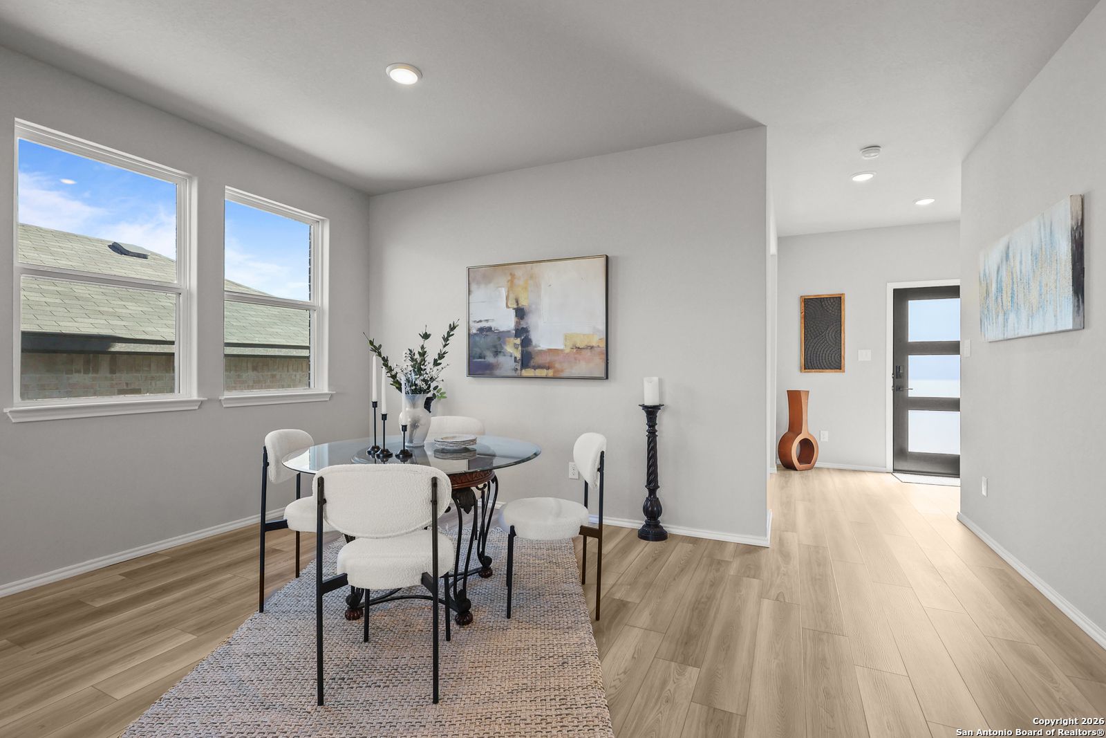 Elegant dining room with round glass table, white chairs, and modern art in Davidson Homes The Murray K, Comanche Ridge, San Antonio