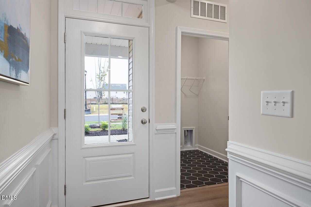 Bright entryway with glass-paneled white front door, wainscoted walls, coat closet, and pet door in Davidson Homes The Carter C, Lillington, NC