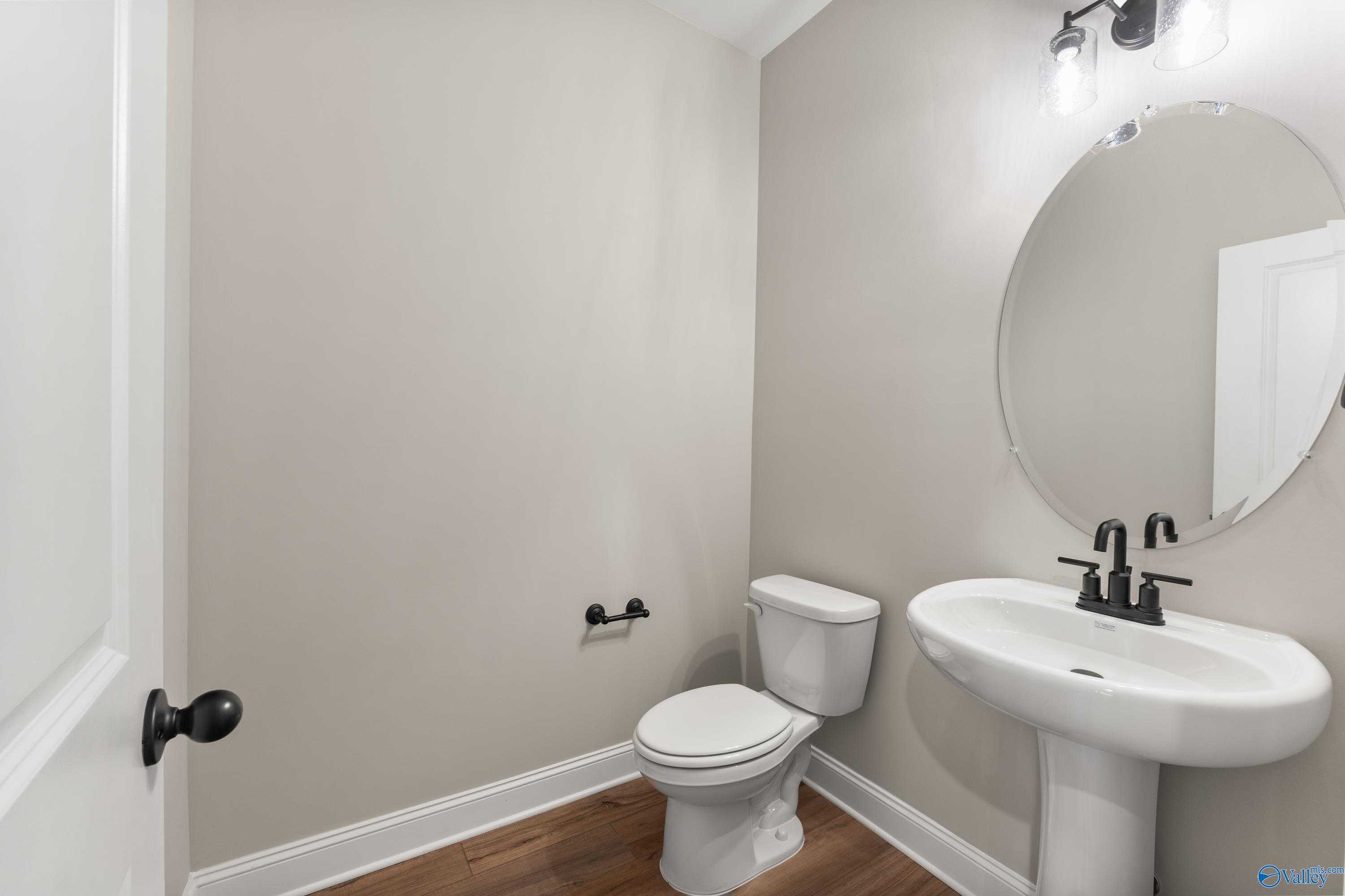 Elegant powder room with round mirror, white pedestal sink, black fixtures in Davidson Homes The Finleigh, Toney, Alabama
