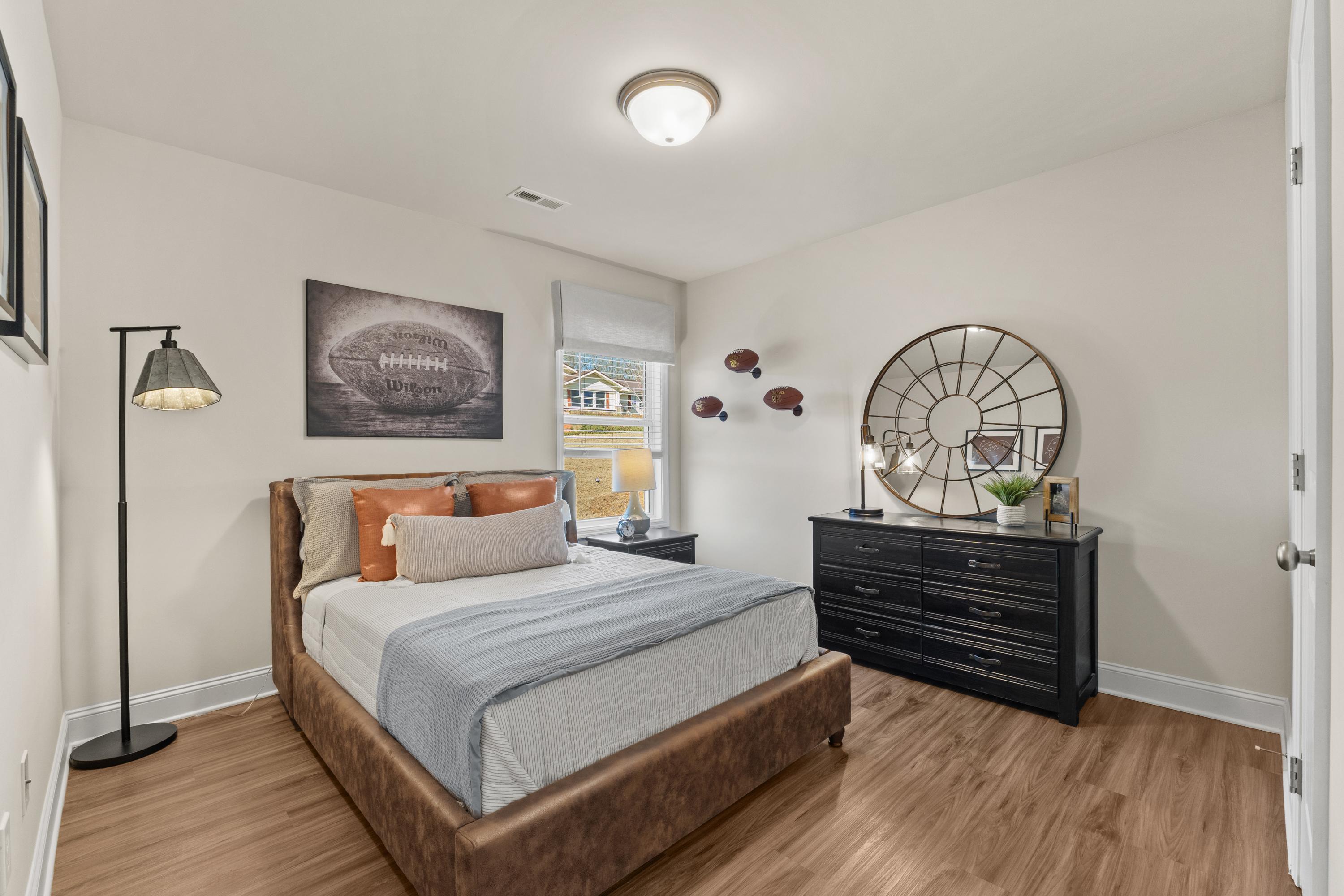 Cozy bedroom in Berry Cove, New Market Alabama with leather bed, hardwood floors, black dresser and football decor