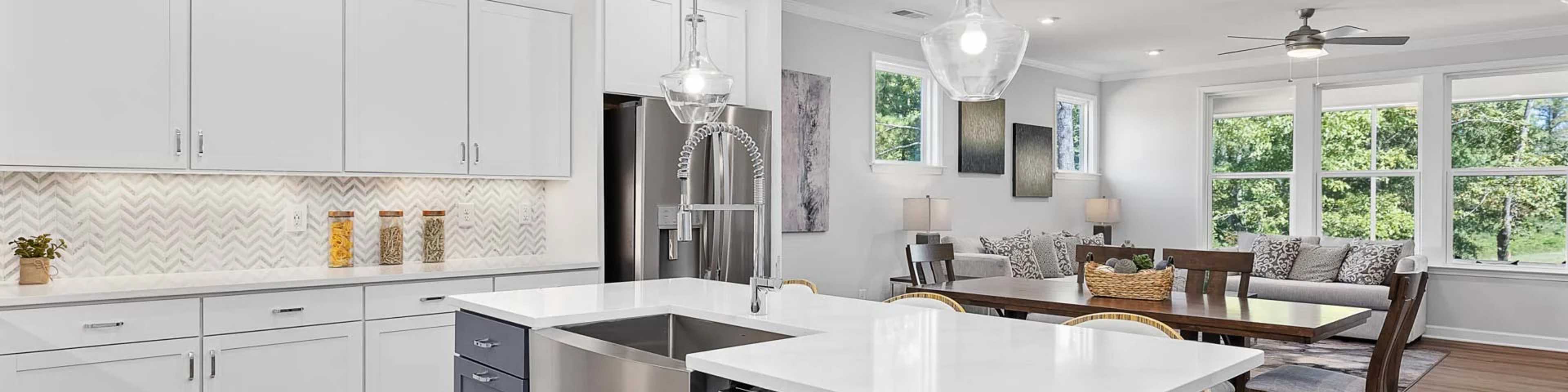 Spacious open-concept kitchen in Belmont new home with white cabinets, navy island, pendant lights, and hardwood floors