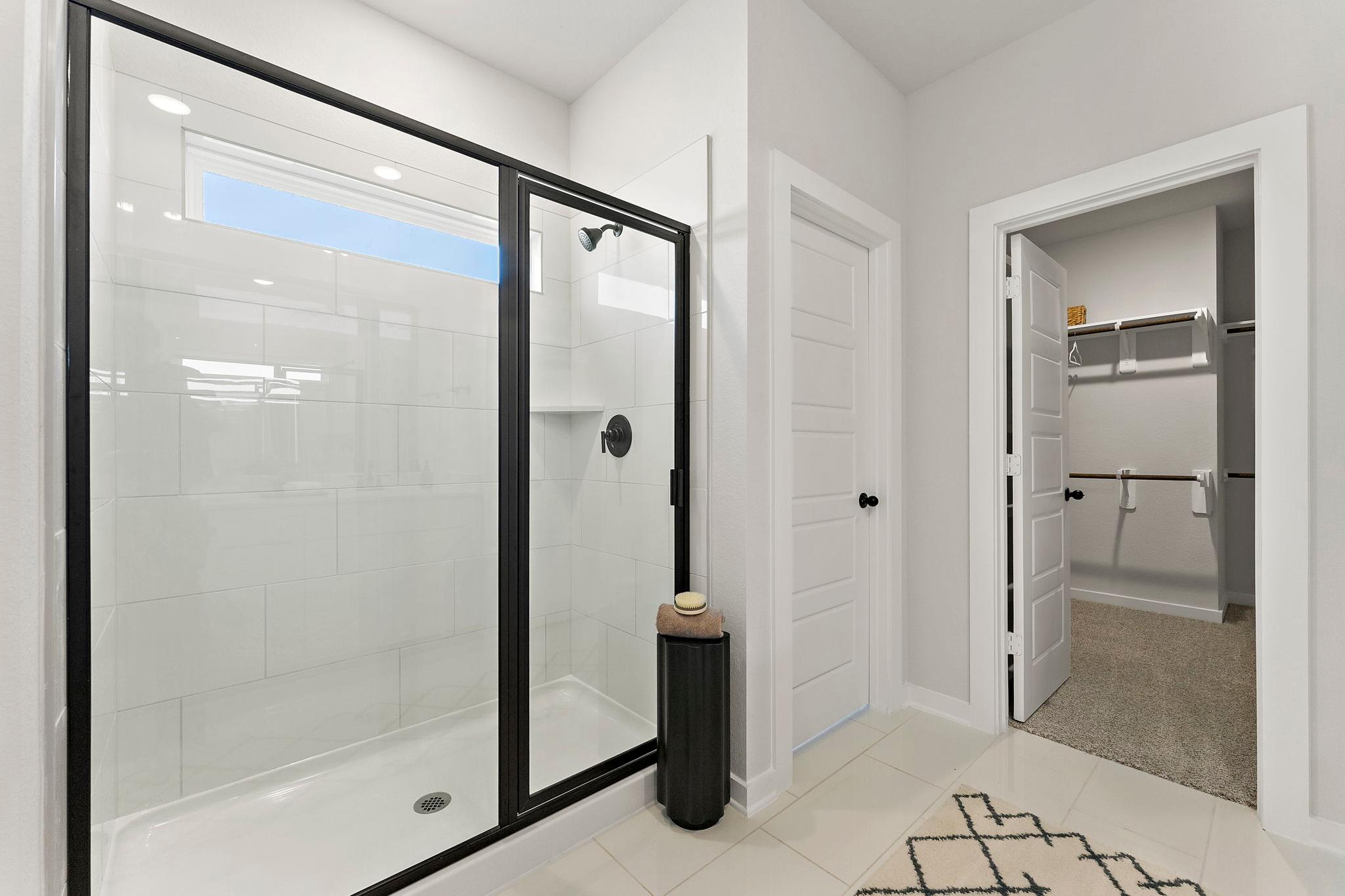Spacious primary bathroom at Sundance Cove in Crosby TX with frameless glass walk-in shower, white subway tiles and adjacent closet