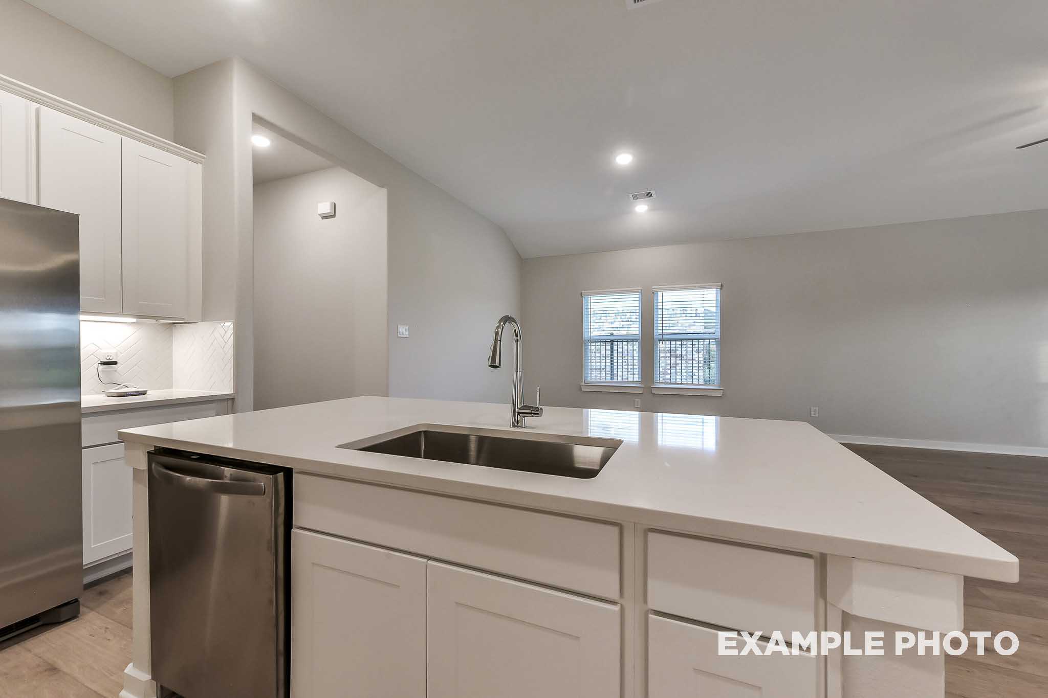 Modern kitchen in The Laguna B featuring white shaker cabinets, large quartz island with farmhouse sink, and stainless steel appliances