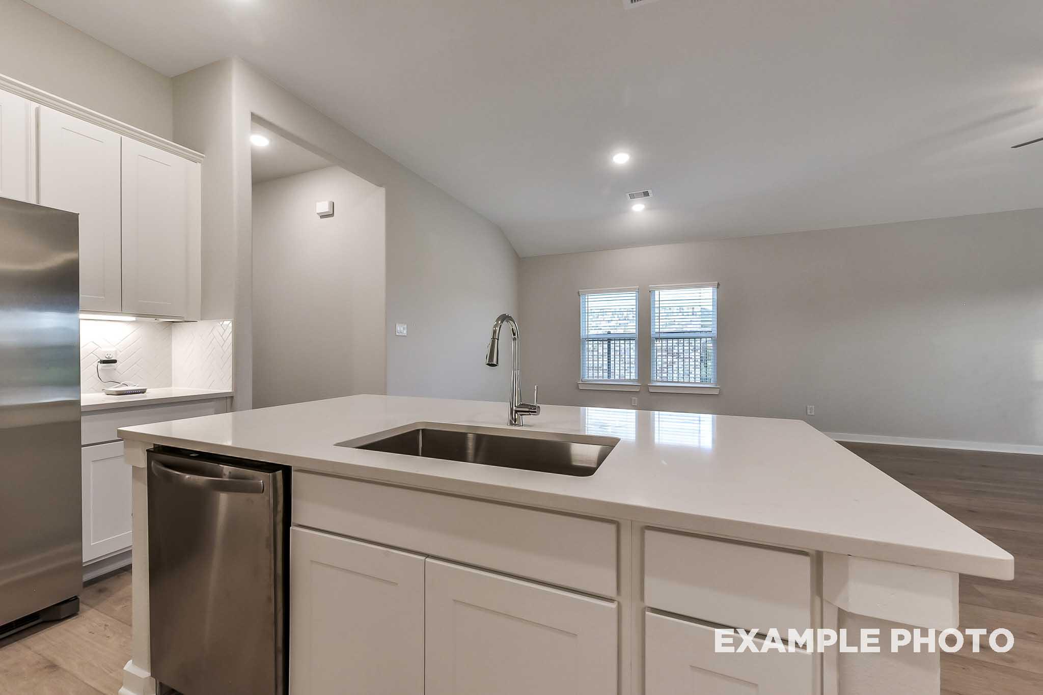 Modern kitchen in The Laguna B featuring white shaker cabinets, large quartz island with farmhouse sink, and stainless steel appliances