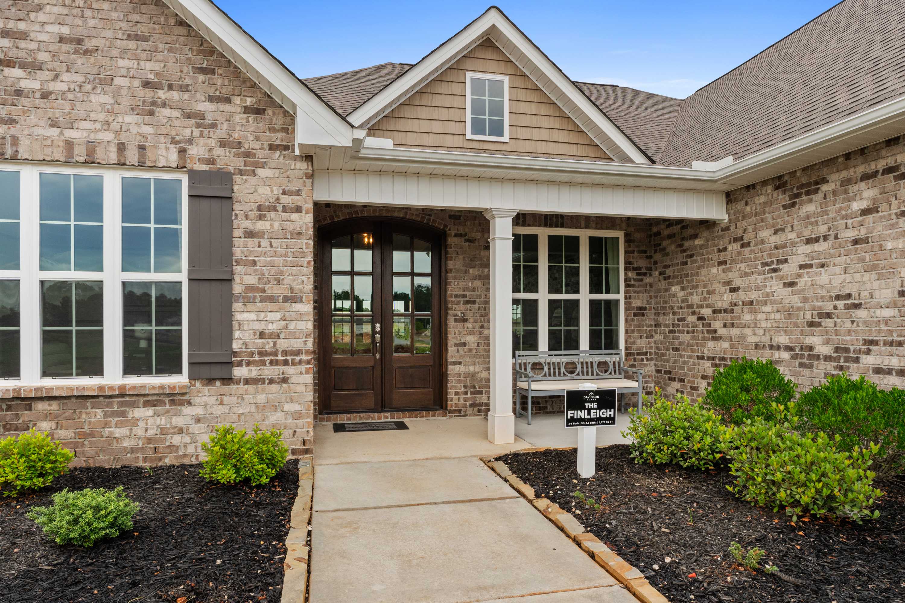 Brick home exterior at Creekside in Harvest Alabama with covered front porch, columns, double doors, and landscaped entry