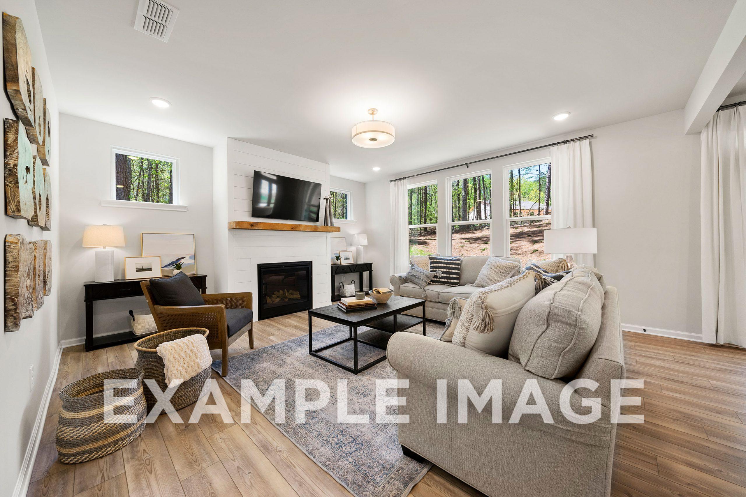 Cozy living room in The Hickory B home with gray sectional sofa, stone fireplace, mounted TV, large windows, and hardwood floors